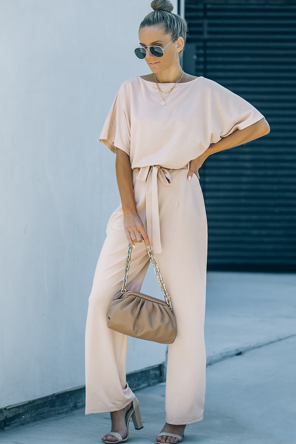 A stylish woman wearing a blue belted wide leg jumpsuit with batwing sleeves, showcasing a chic and glamorous look.