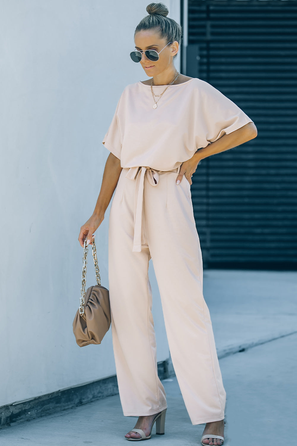 A stylish woman wearing a blue belted wide leg jumpsuit with batwing sleeves, showcasing a chic and glamorous look.