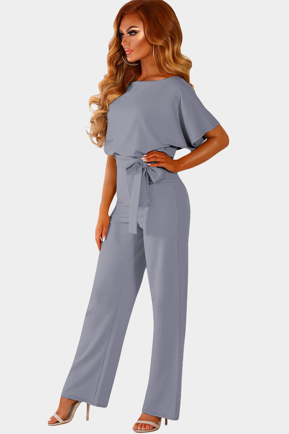 A stylish woman wearing a blue belted wide leg jumpsuit with batwing sleeves, showcasing a chic and glamorous look.