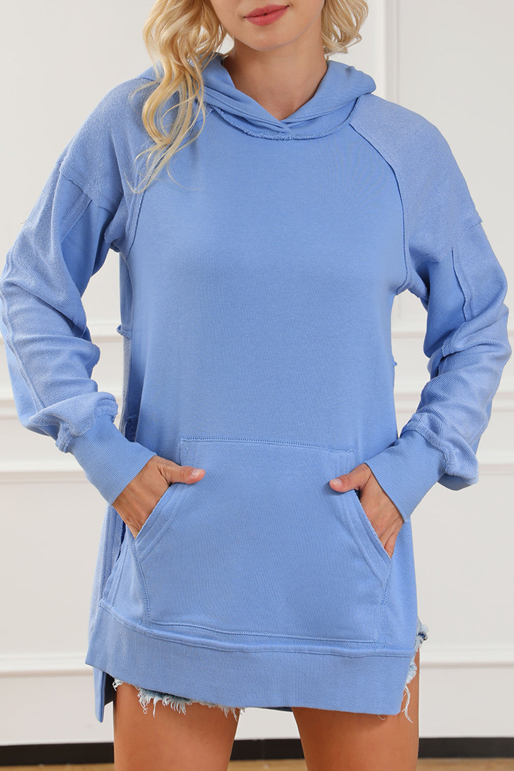 A stylish blue tunic hoodie featuring raw seams, patchwork design, and a kangaroo pocket, perfect for casual wear.