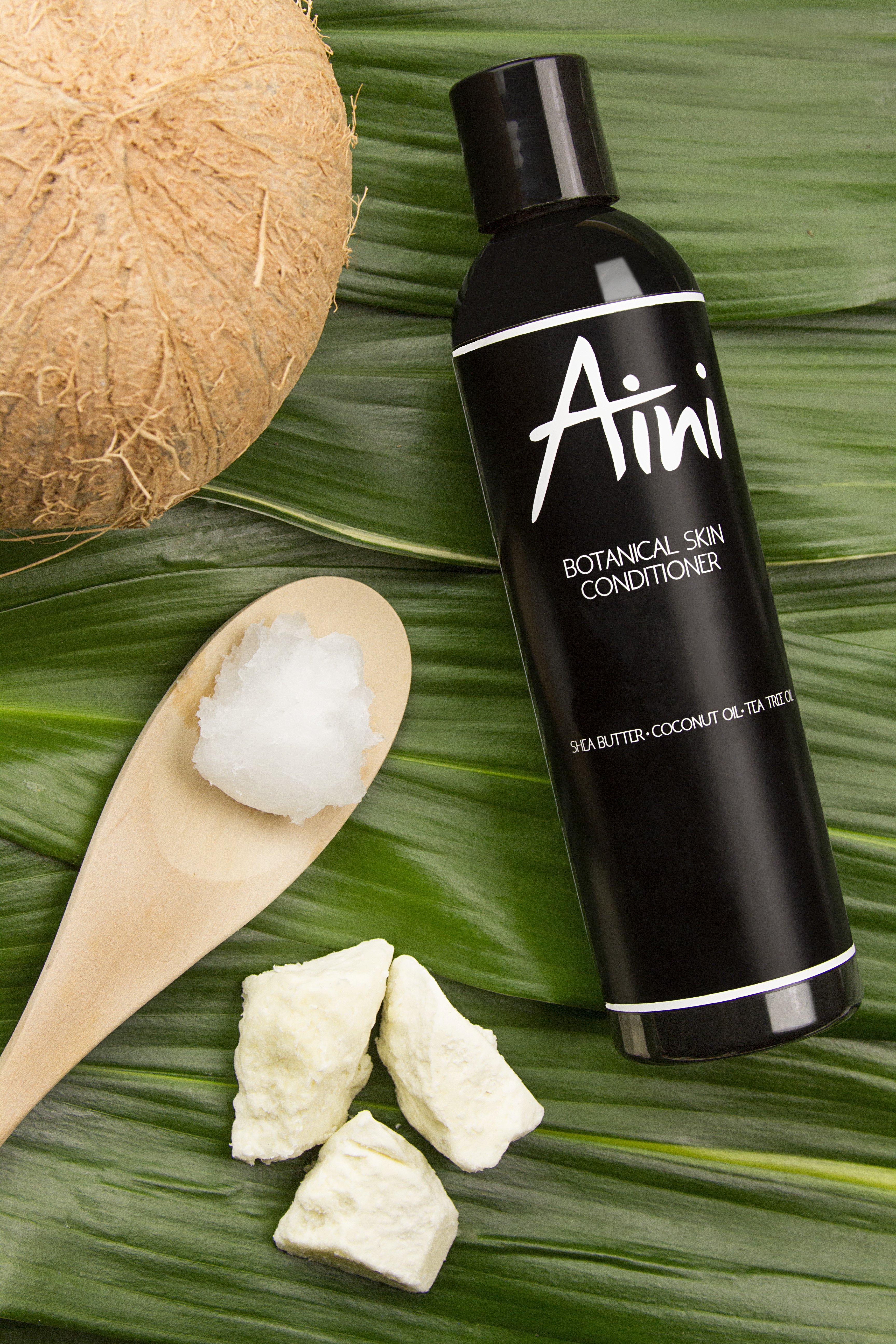 A bottle of Botanical Skin Conditioner featuring a lightweight formula with tea tree oil and shea butter, surrounded by natural ingredients like coconut oil and vanilla beans.