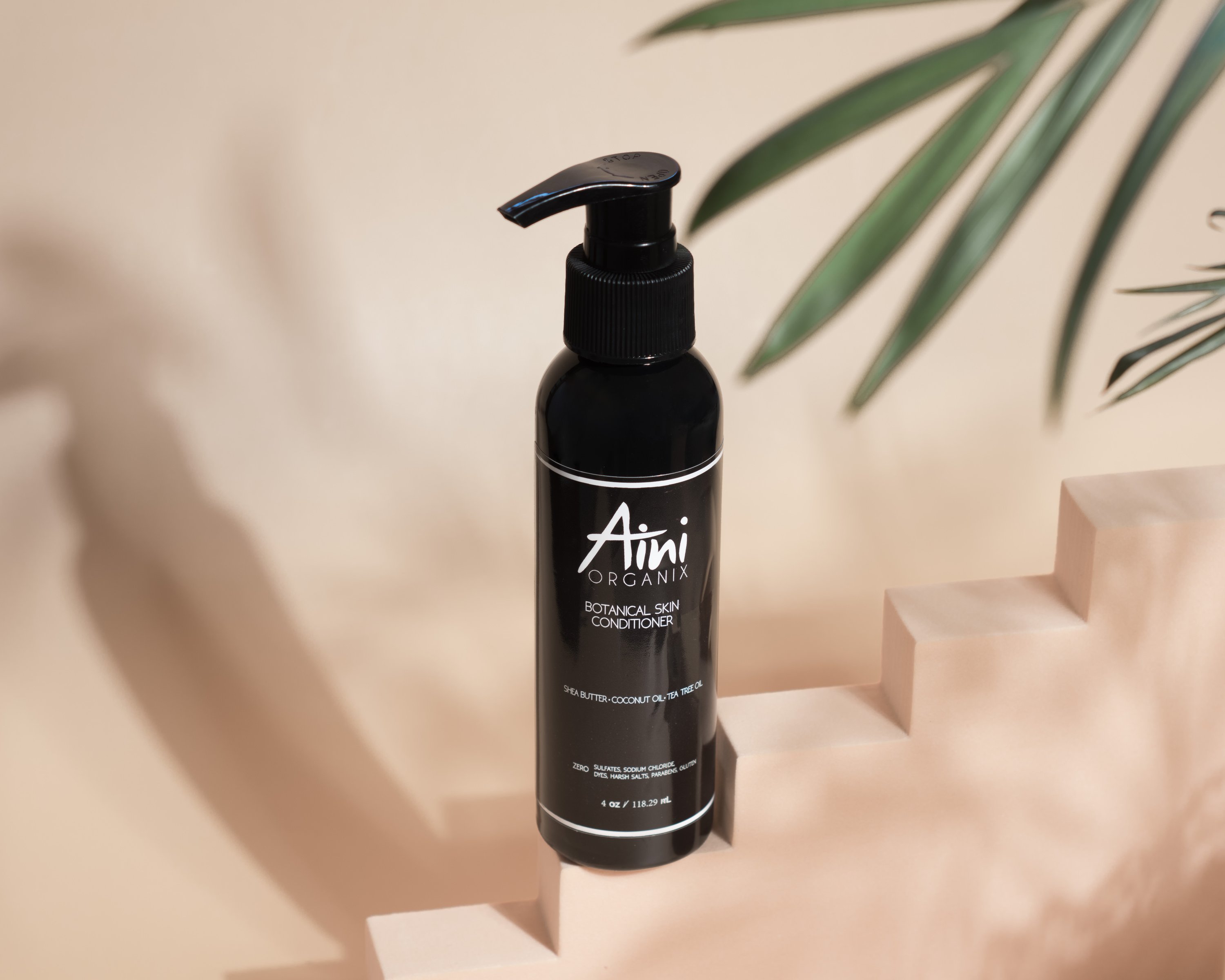 A bottle of Botanical Skin Conditioner featuring a lightweight formula with tea tree oil and shea butter, surrounded by natural ingredients like coconut oil and vanilla beans.