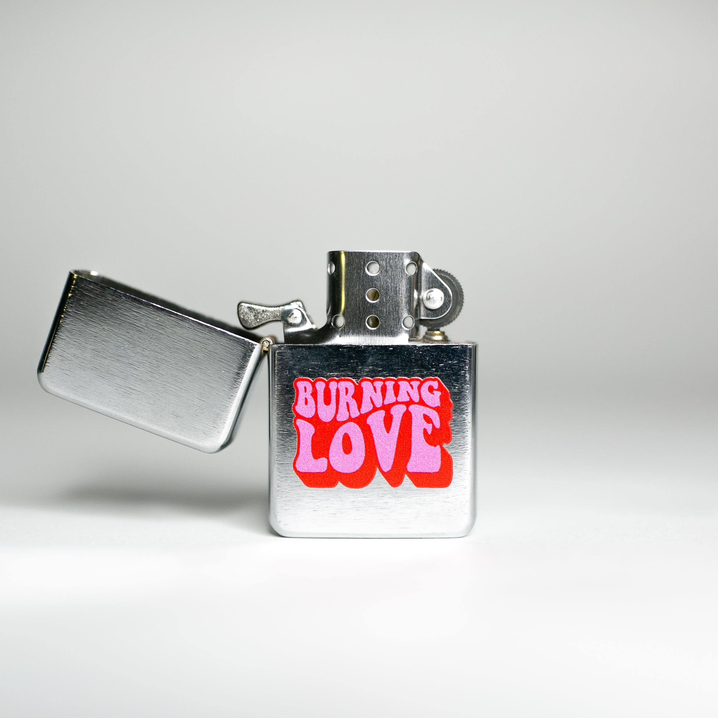 A stylish silver-brushed metal lighter named 'Burning Love', featuring a spring action flip top and compact design, perfect for Elvis fans.