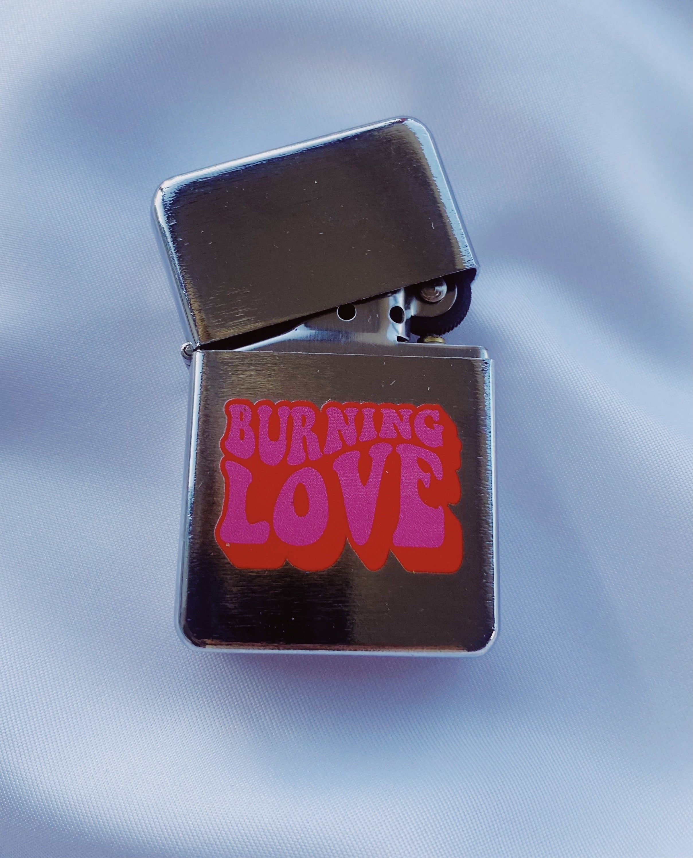 A stylish silver-brushed metal lighter named 'Burning Love', featuring a spring action flip top and compact design, perfect for Elvis fans.