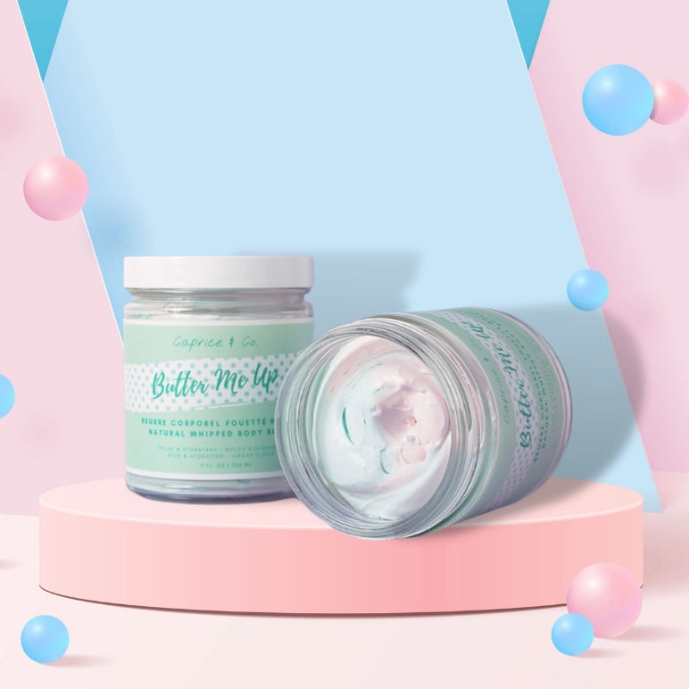 A jar of Butter Me Up Cotton Candy Body Butter with a creamy texture and a light pink color, surrounded by cotton candy fluff.