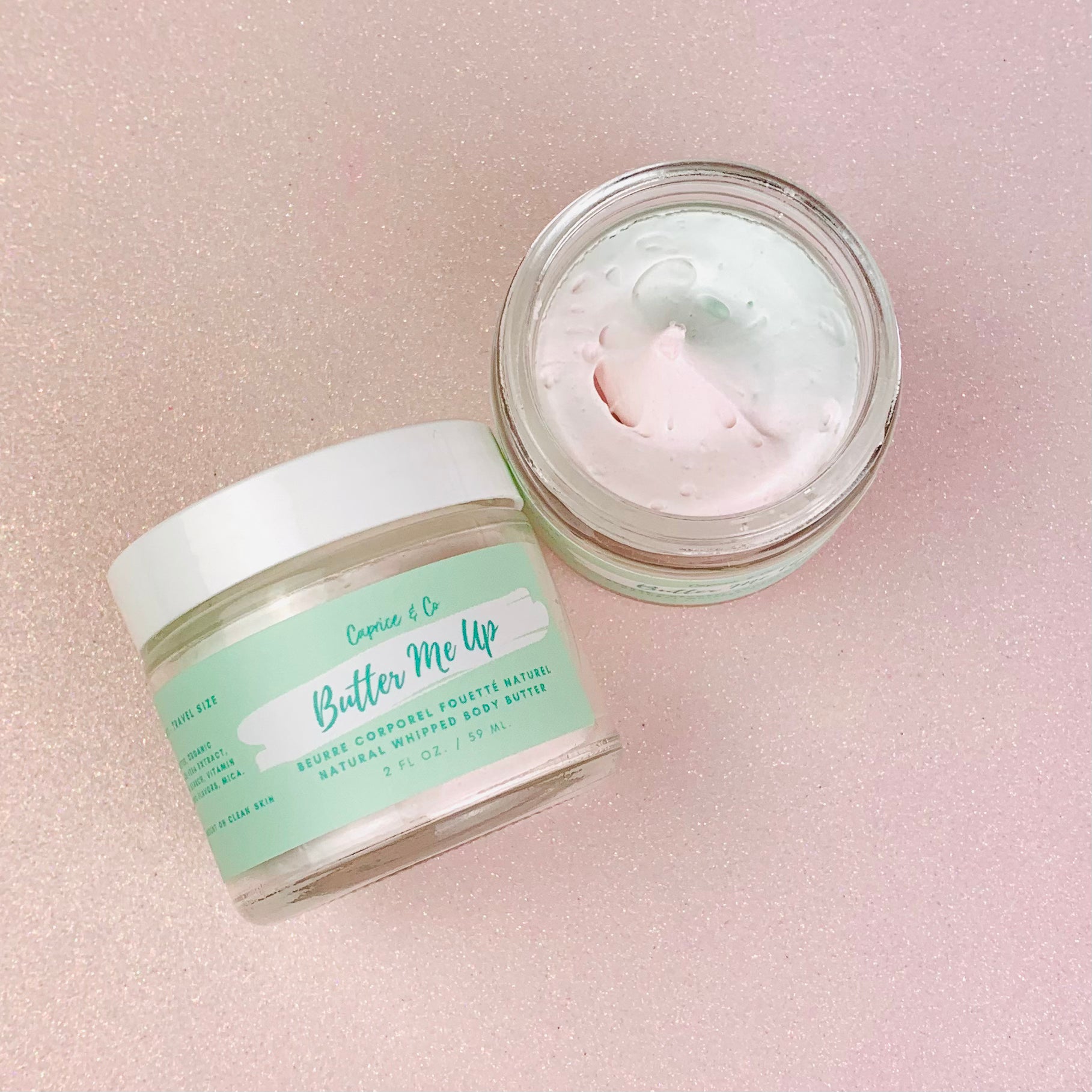 A jar of Butter Me Up Cotton Candy Body Butter with a creamy texture and a light pink color, surrounded by cotton candy fluff.