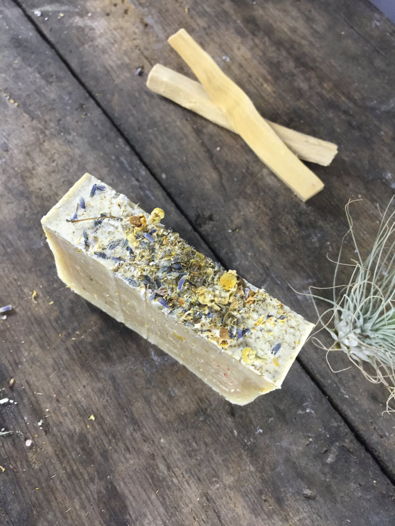 A beautifully handcrafted vegan soap bar infused with organic lavender and chamomile, topped with dried lavender flowers and chamomile buds, showcasing its natural ingredients.