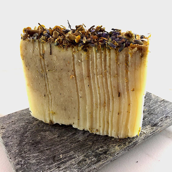 A beautifully handcrafted vegan soap bar infused with organic lavender and chamomile, topped with dried lavender flowers and chamomile buds, showcasing its natural ingredients.