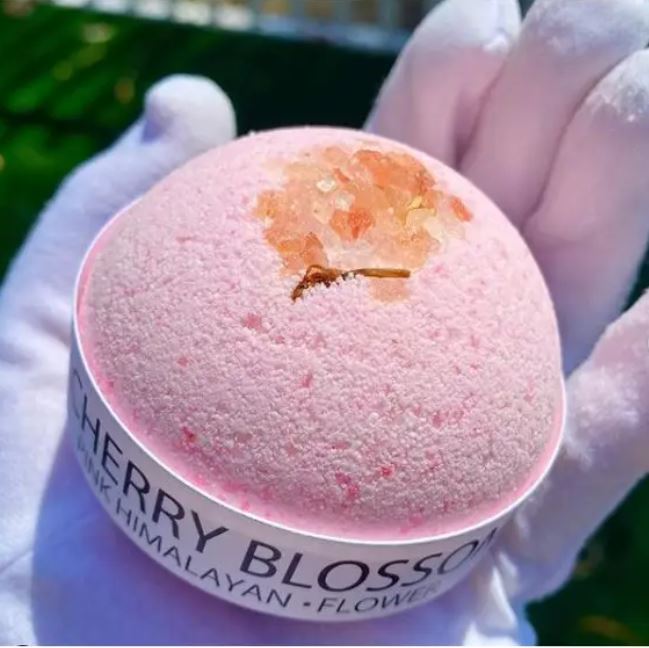 Cherry Blossom and Himalayan Salt Bath Bomb in a pink hue, surrounded by delicate cherry blossoms, showcasing its luxurious and soothing properties.