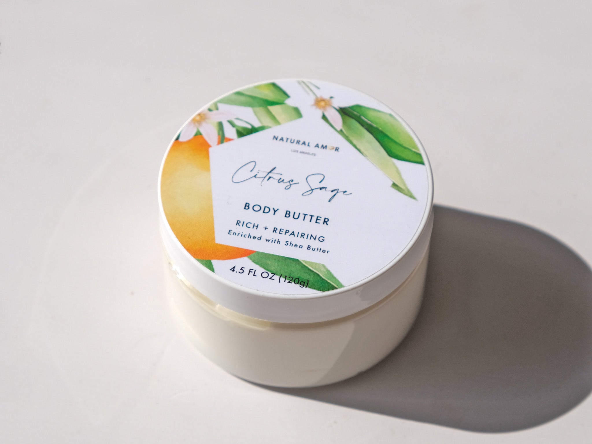 Citrus Sage Emulsified Body Butter in a jar, showcasing its creamy texture and vibrant citrus color, surrounded by fresh citrus fruits and sage leaves.