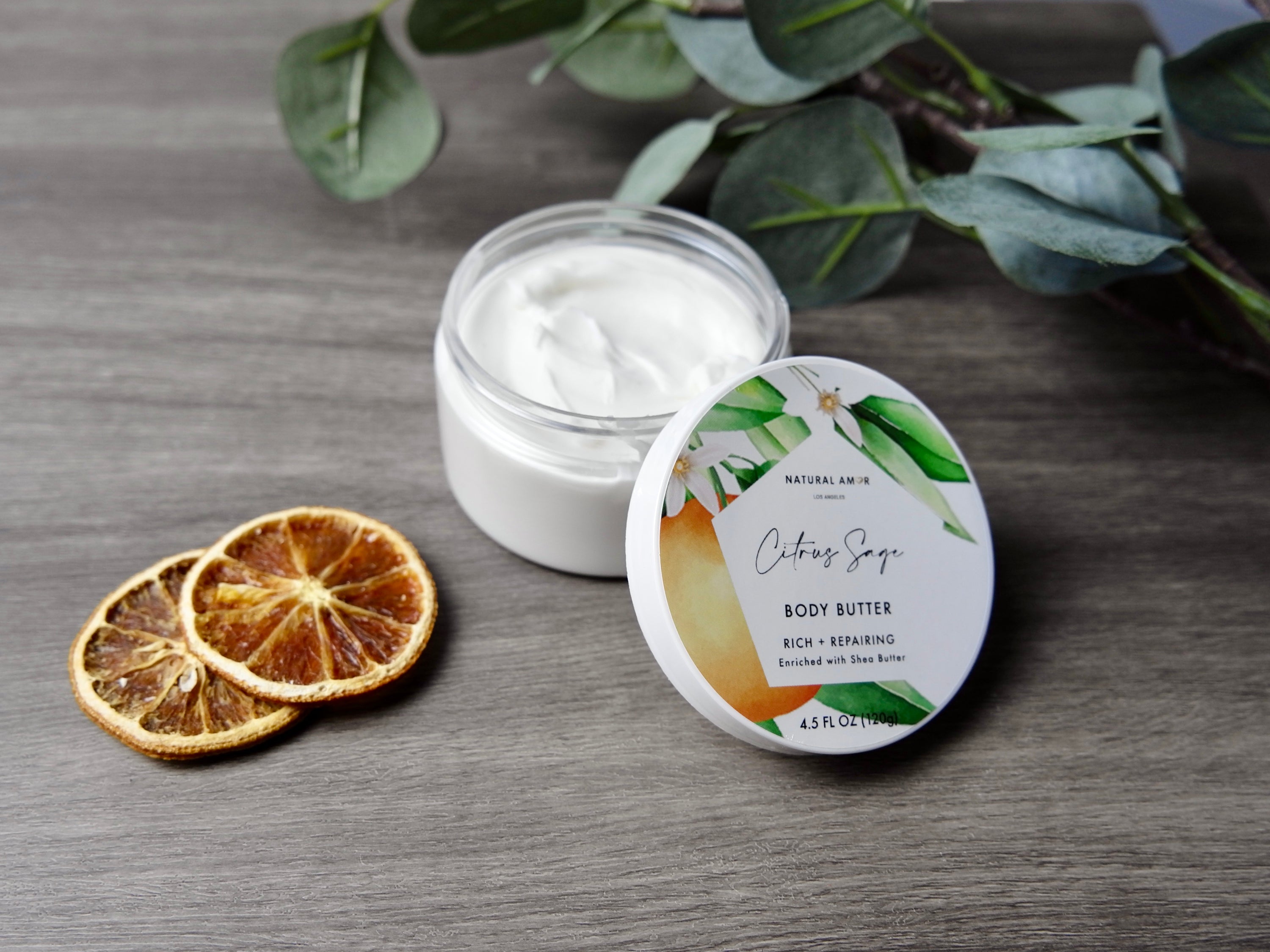 Citrus Sage Emulsified Body Butter in a jar, showcasing its creamy texture and vibrant citrus color, surrounded by fresh citrus fruits and sage leaves.