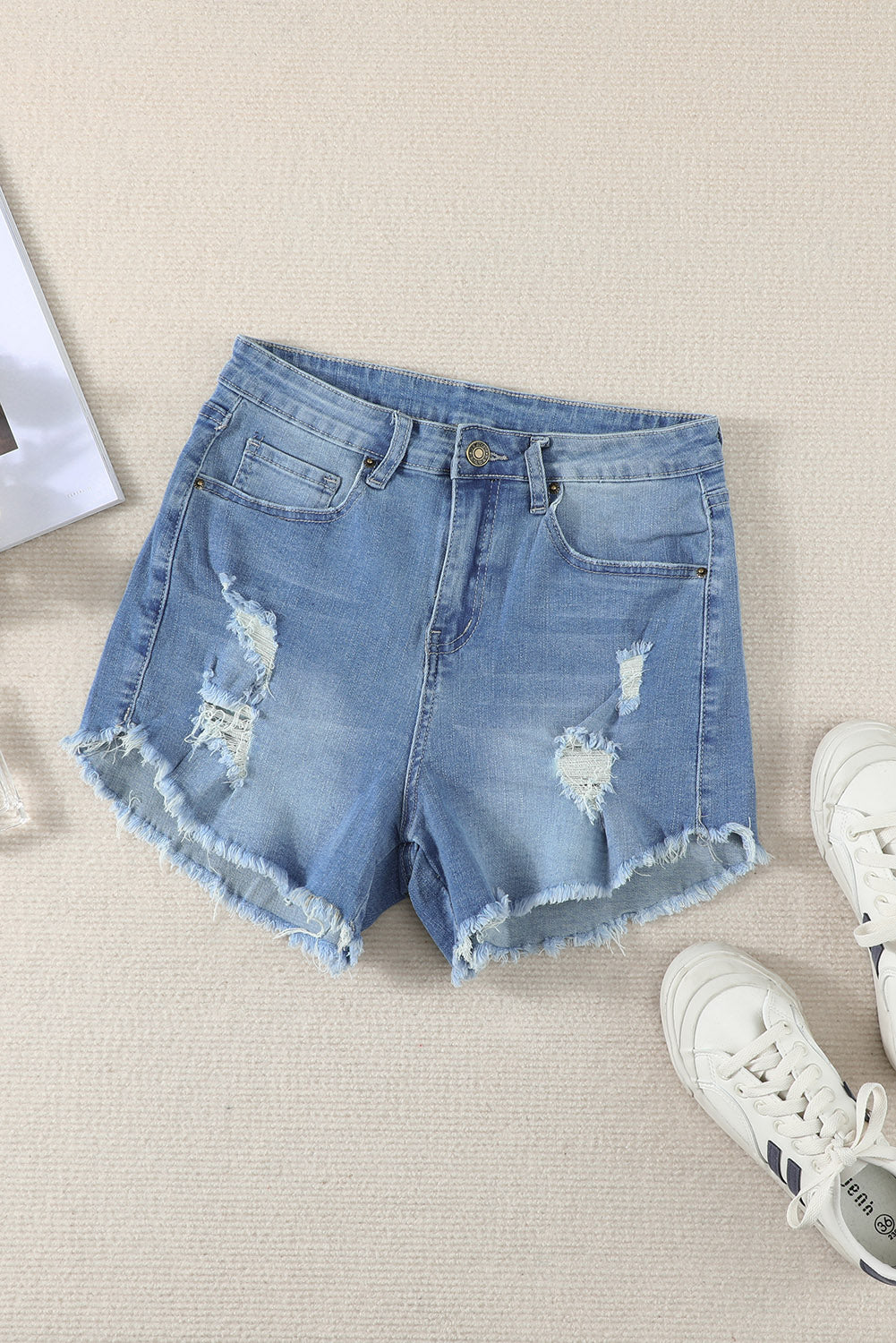 A pair of dark blue frayed hem denim shorts displayed on a white background, showcasing the stylish distressed design and pockets.