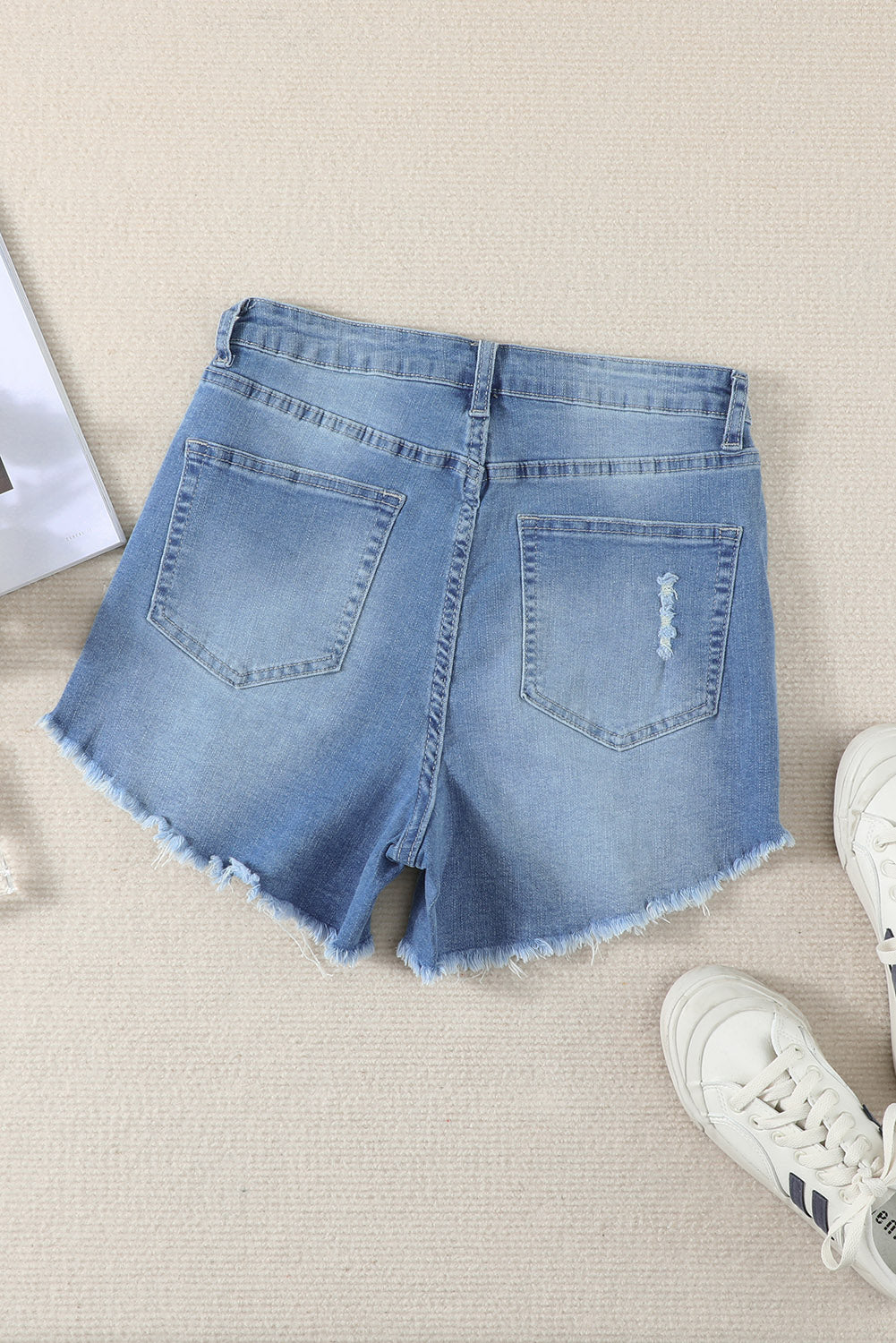 A pair of dark blue frayed hem denim shorts displayed on a white background, showcasing the stylish distressed design and pockets.