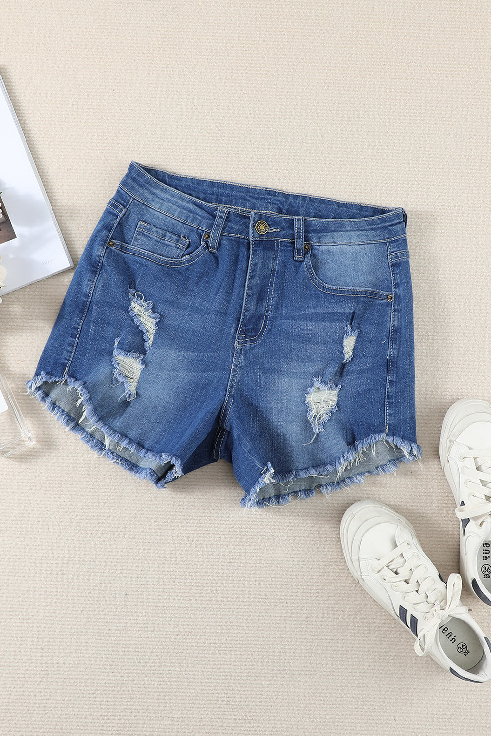 A pair of dark blue frayed hem denim shorts displayed on a white background, showcasing the stylish distressed design and pockets.