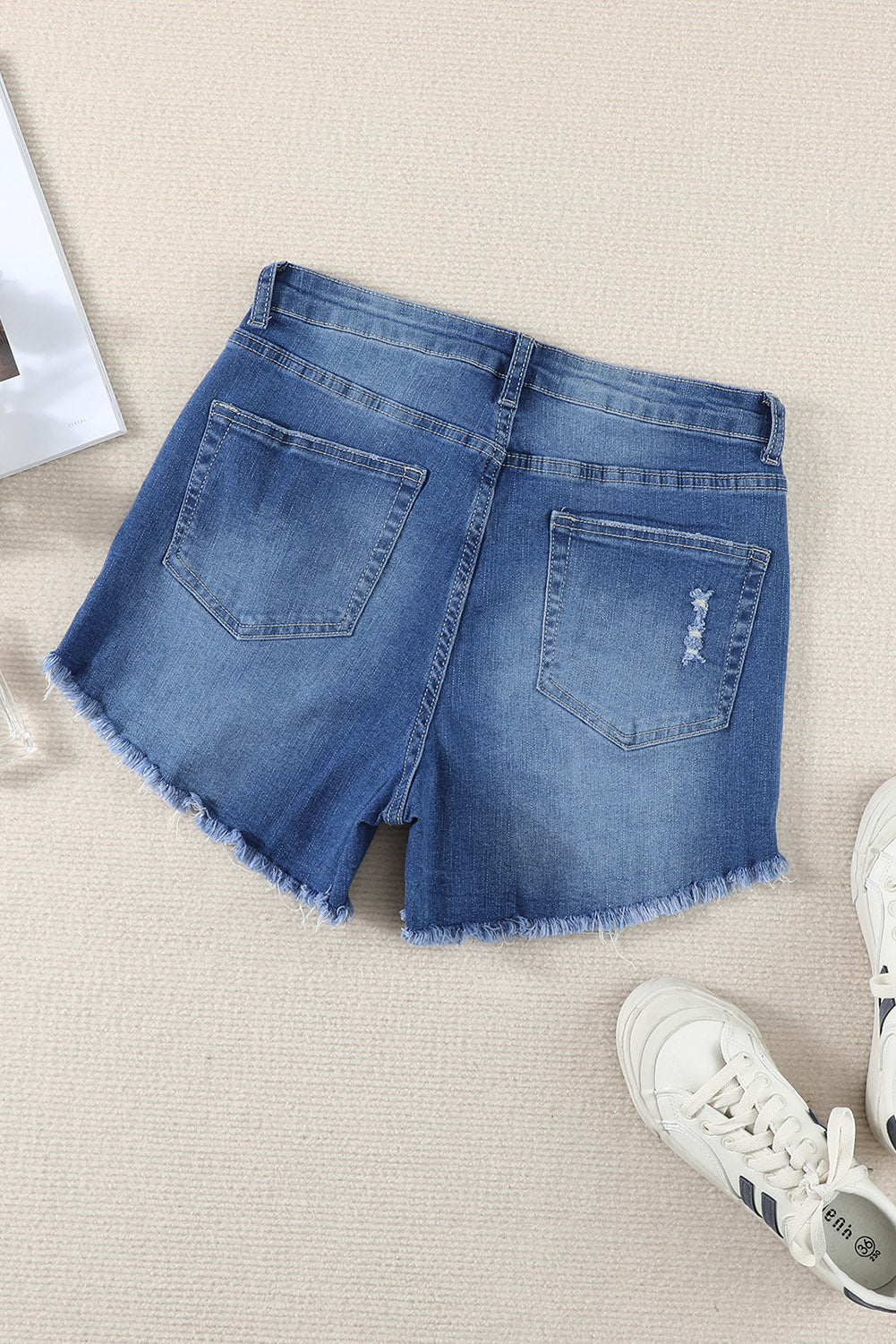 A pair of dark blue frayed hem denim shorts displayed on a white background, showcasing the stylish distressed design and pockets.