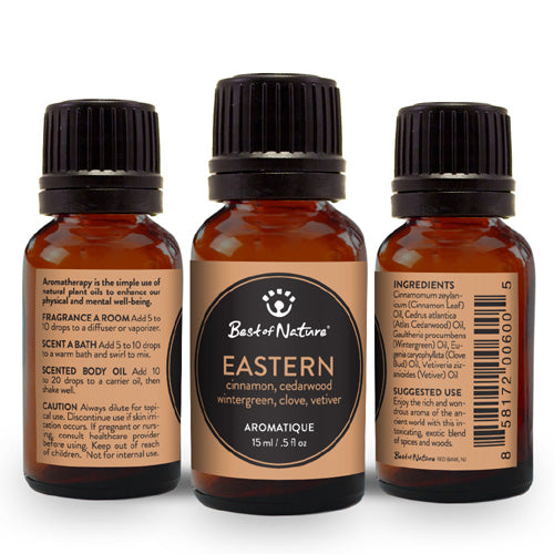 A bottle of Eastern Aromatique Essential Oil Blend featuring a rich amber color, surrounded by cinnamon sticks, cedarwood pieces, and green vetiver grass.