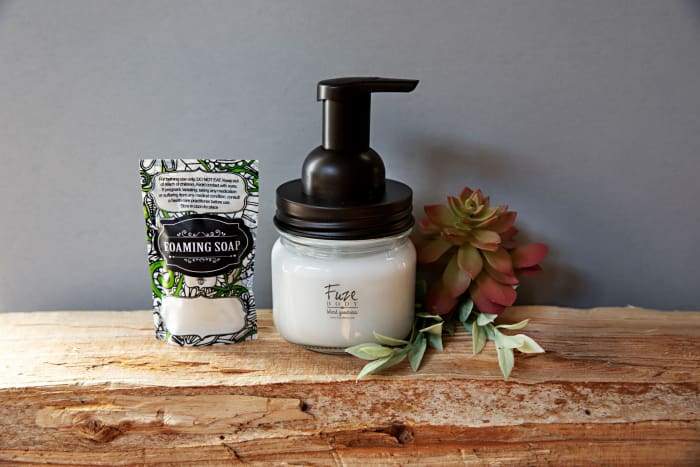 A stylish reusable glass foaming soap jar filled with natural essential oil hand soap, featuring a blend of organic ingredients and essential oils.