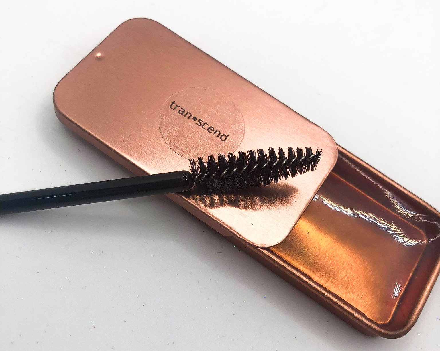 A stylish rose gold tin of Glazed Brow Soap with a spoolie brush, showcasing its clear texture and nourishing ingredients.