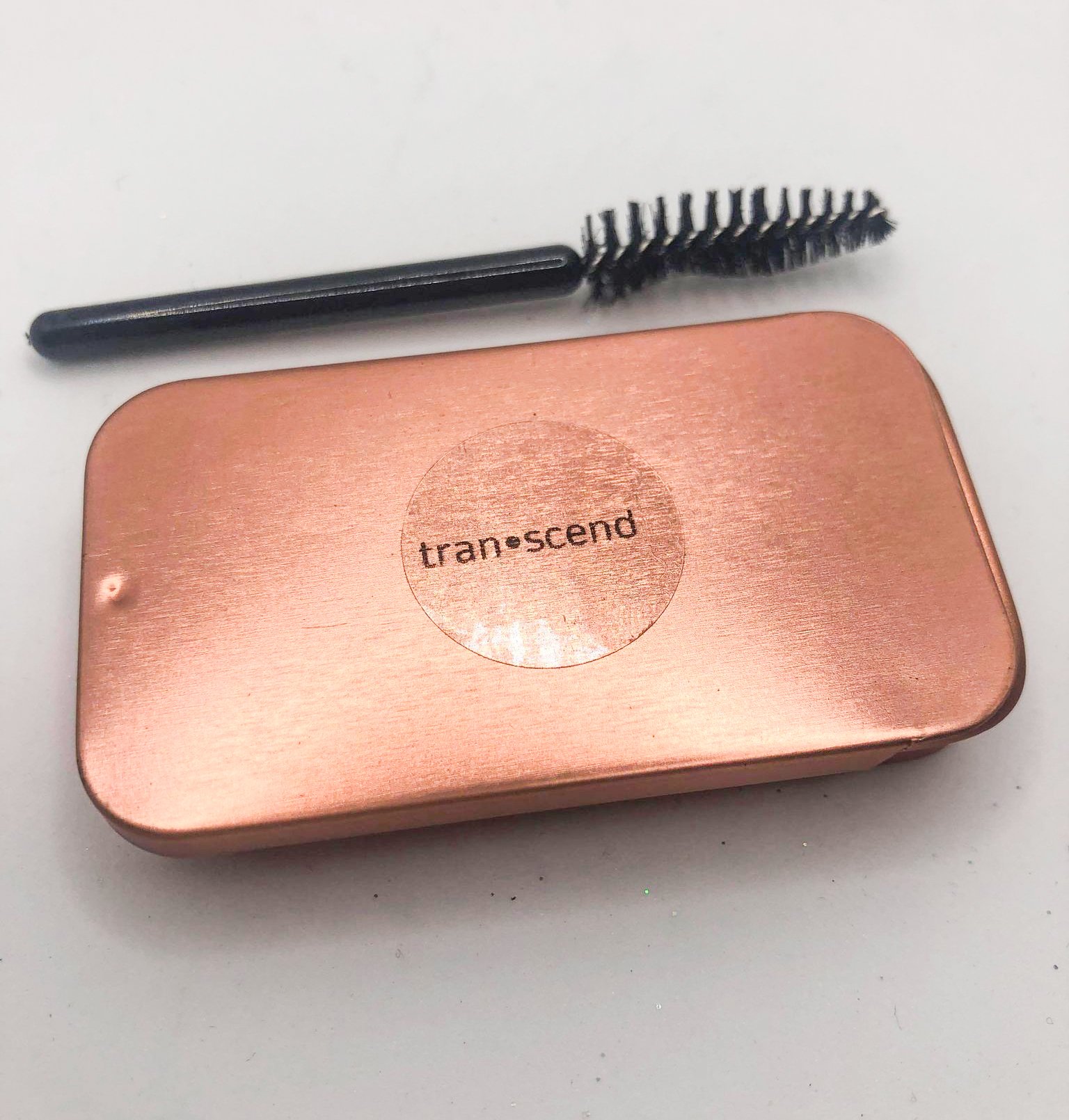 A stylish rose gold tin of Glazed Brow Soap with a spoolie brush, showcasing its clear texture and nourishing ingredients.