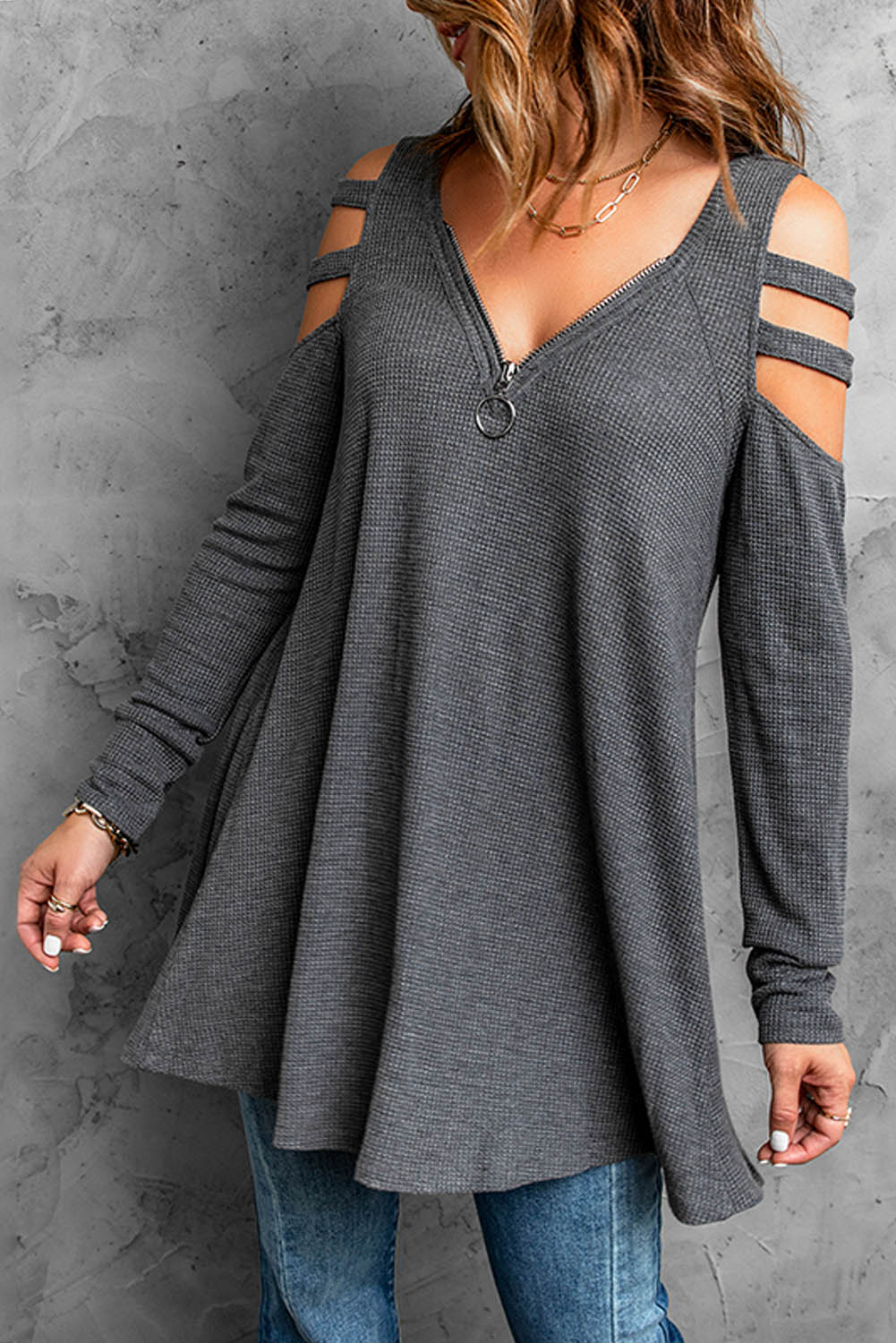 Gray long sleeve top with zip neck and cut-out design, featuring a textured waffle knit fabric and a loose fit with a ruffled hemline.