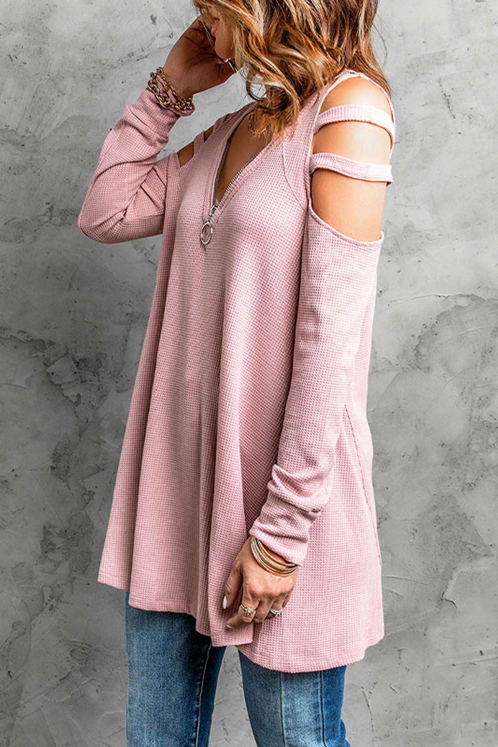 Gray long sleeve top with zip neck and cut-out design, featuring a textured waffle knit fabric and a loose fit with a ruffled hemline.