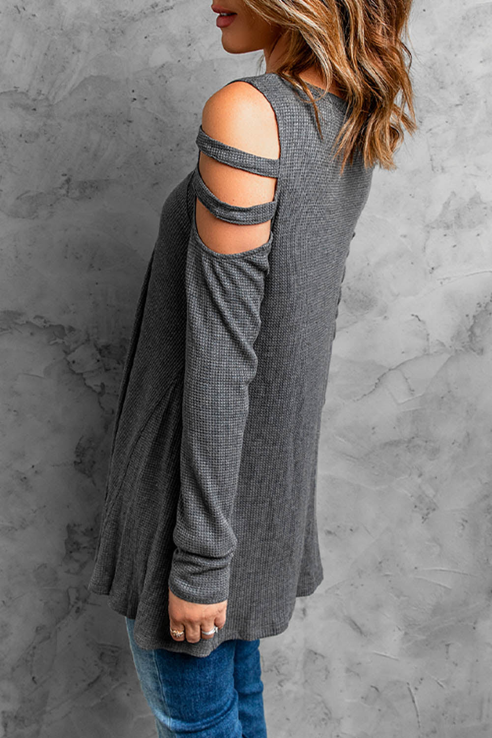 Gray long sleeve top with zip neck and cut-out design, featuring a textured waffle knit fabric and a loose fit with a ruffled hemline.