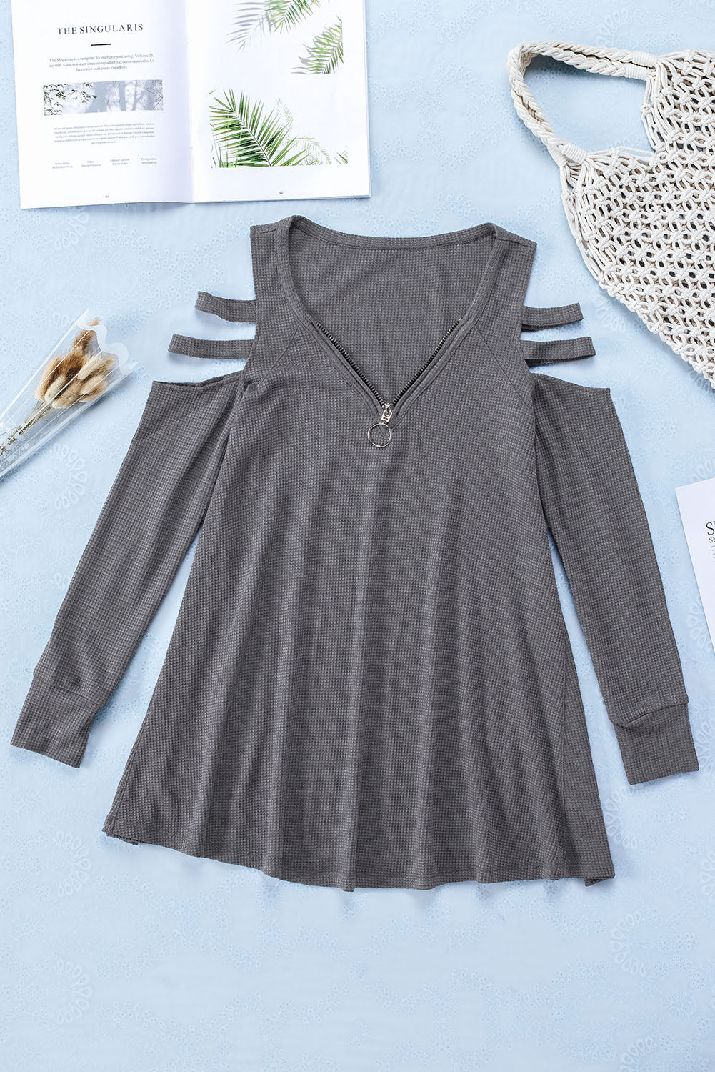 Gray long sleeve top with zip neck and cut-out design, featuring a textured waffle knit fabric and a loose fit with a ruffled hemline.