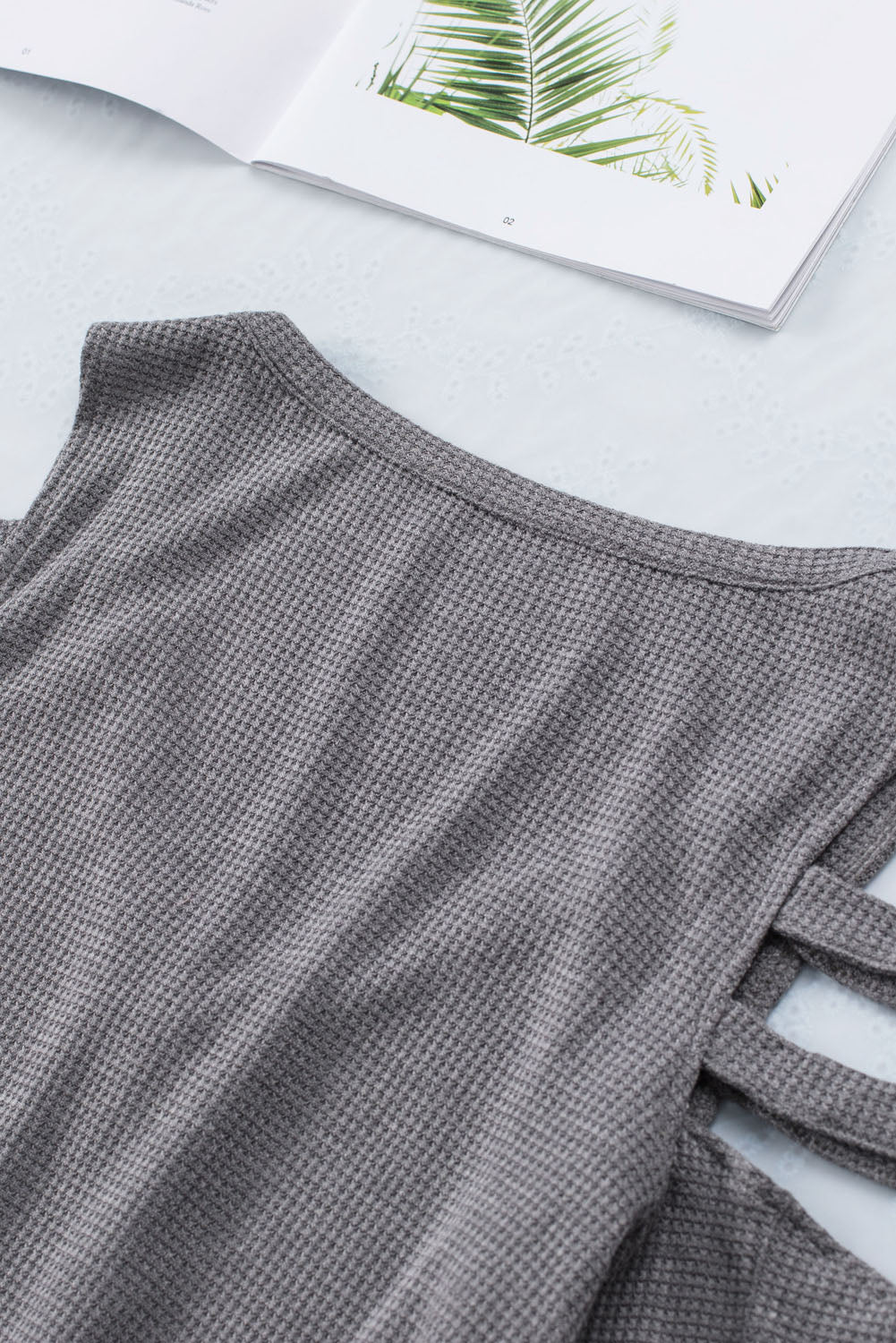 Gray long sleeve top with zip neck and cut-out design, featuring a textured waffle knit fabric and a loose fit with a ruffled hemline.