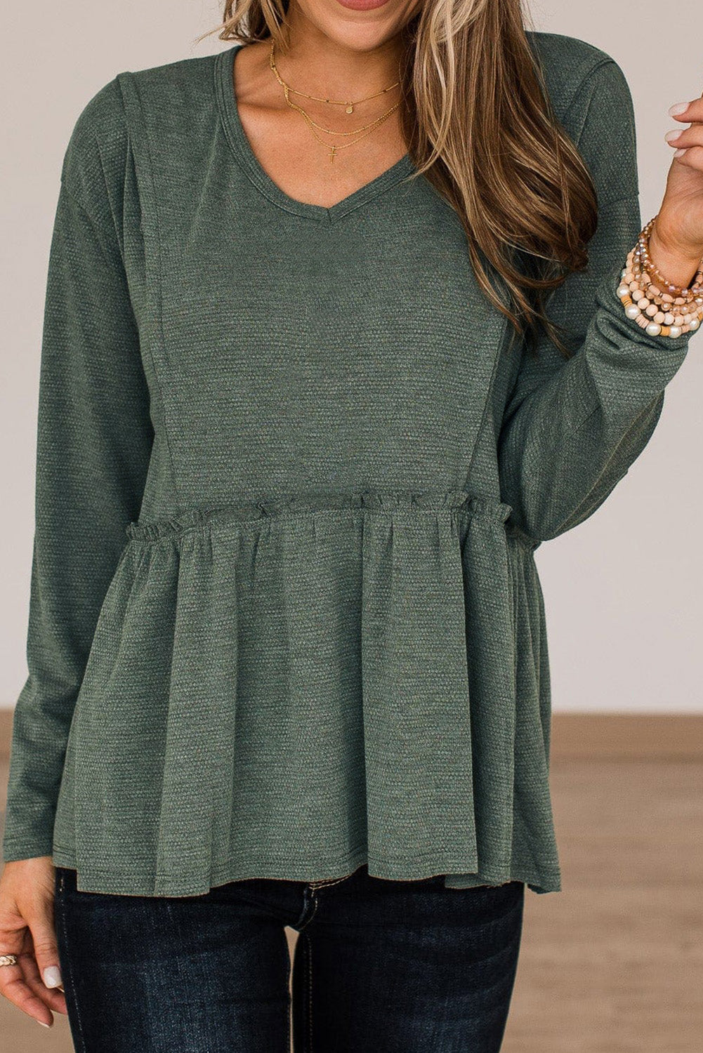 A stylish green long sleeve peplum top featuring outseam details and a ruffle trimmed waistline, perfect for casual and chic outfits.