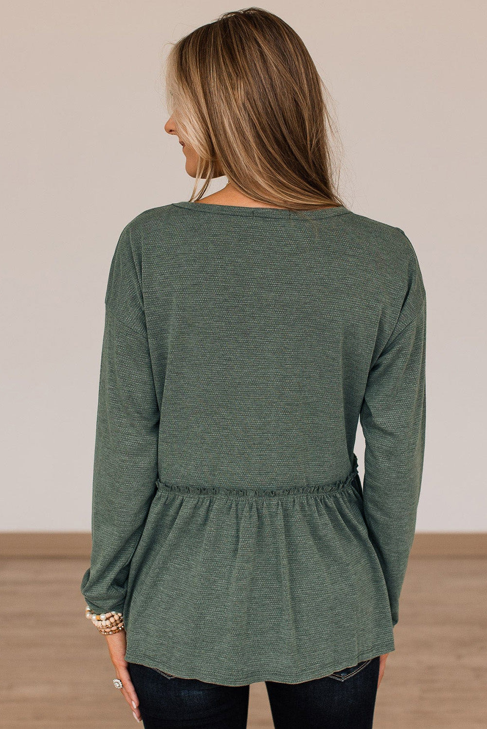 A stylish green long sleeve peplum top featuring outseam details and a ruffle trimmed waistline, perfect for casual and chic outfits.