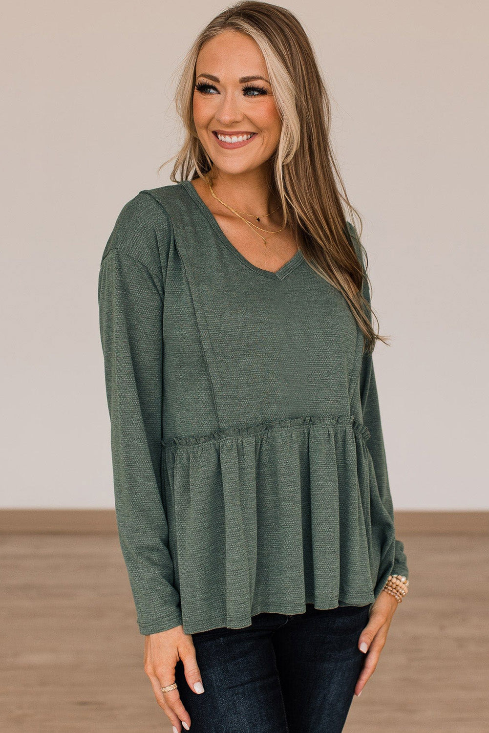 A stylish green long sleeve peplum top featuring outseam details and a ruffle trimmed waistline, perfect for casual and chic outfits.