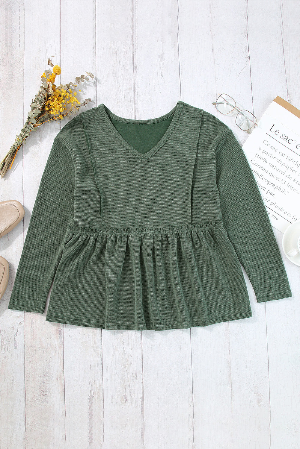 A stylish green long sleeve peplum top featuring outseam details and a ruffle trimmed waistline, perfect for casual and chic outfits.