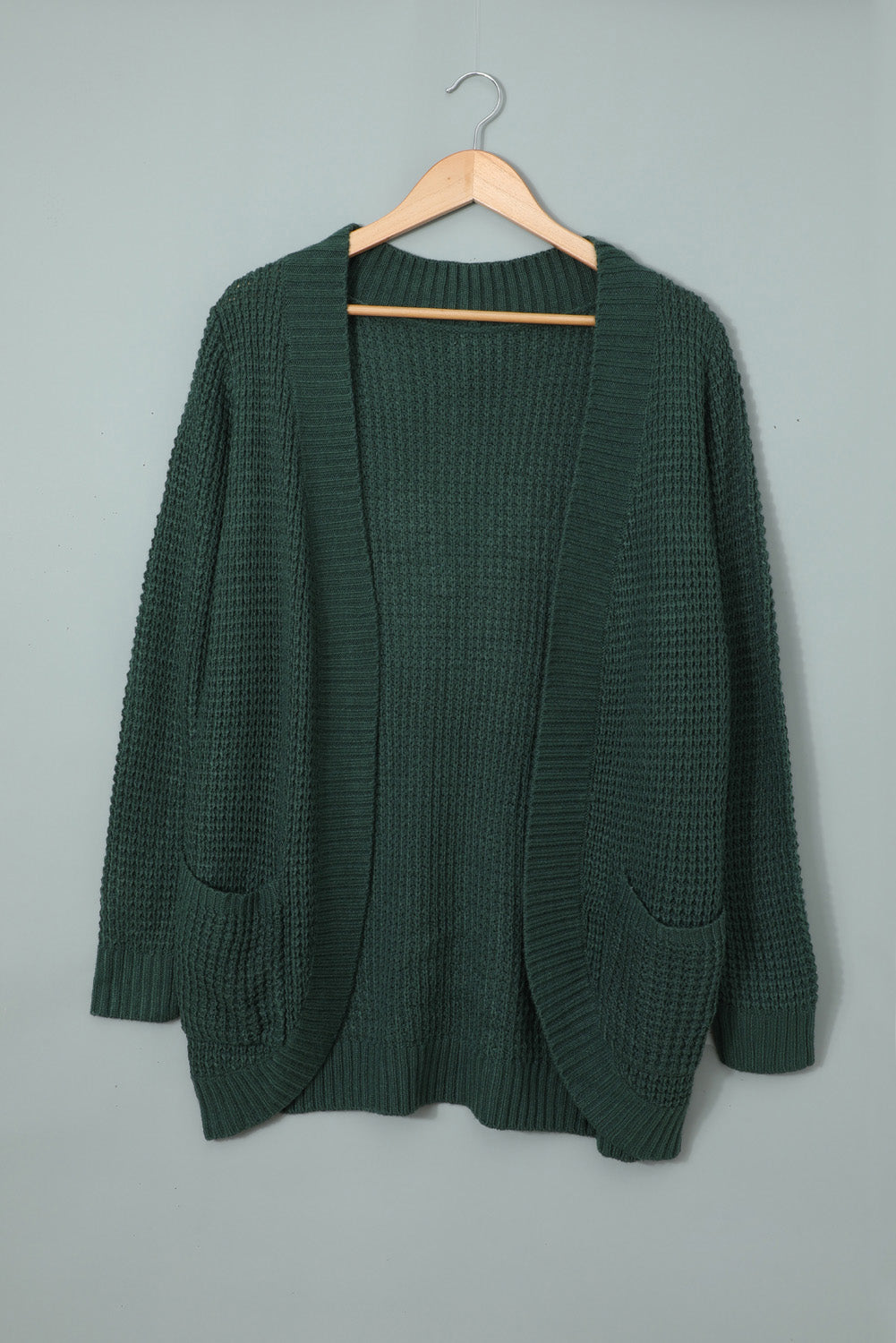 A stylish green pocket knitted solid color cardigan with a fuzzy texture and arc-shaped hem design, perfect for casual wear.