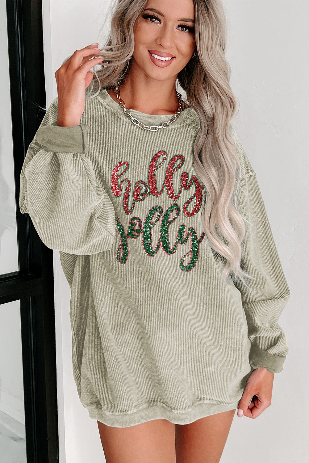 A vibrant green corded sweatshirt featuring a sequined 'holly jolly' graphic, perfect for festive occasions.