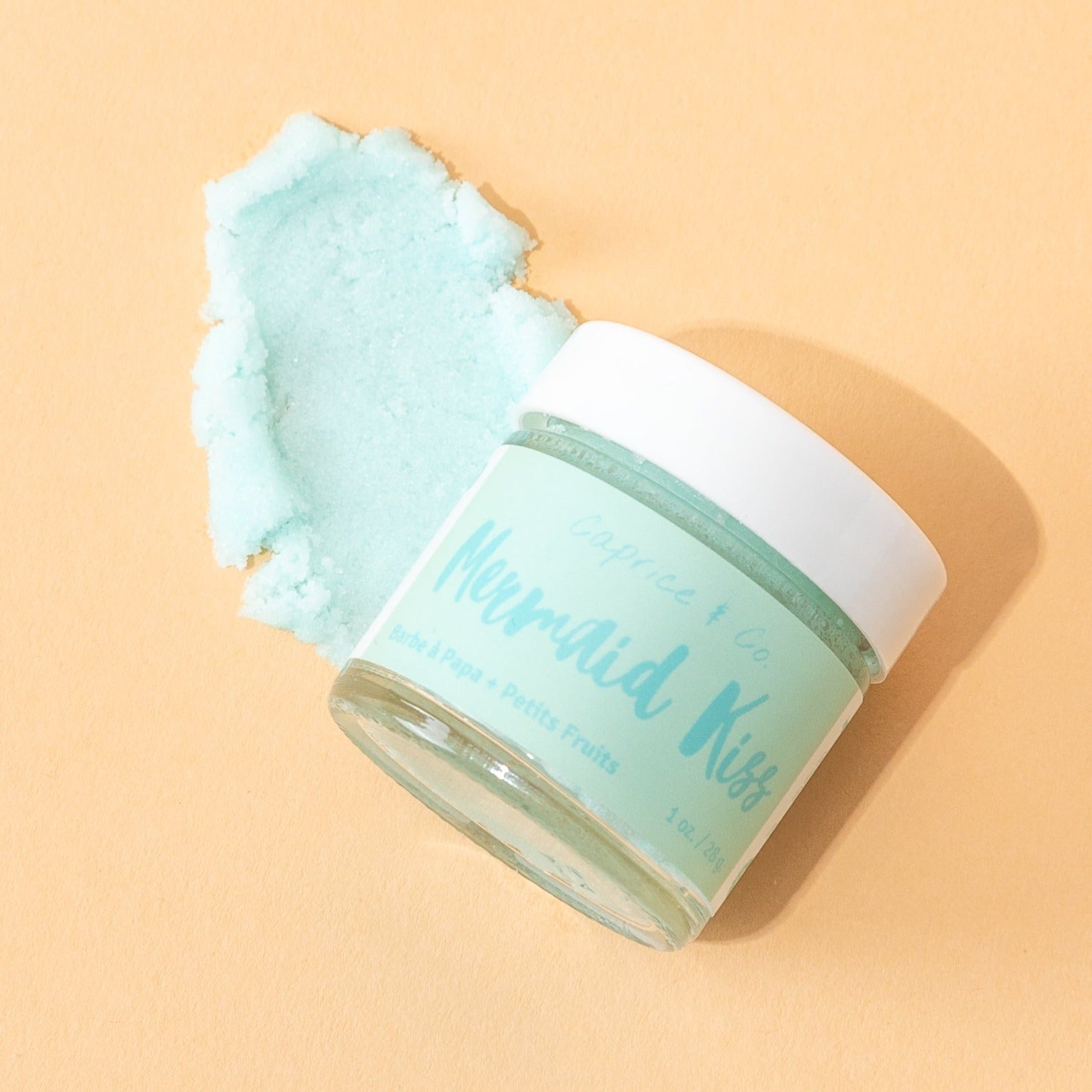 Mermaid Kiss Lip Scrub in a jar, featuring a vibrant cotton candy and berry color, with a spoon beside it for application.