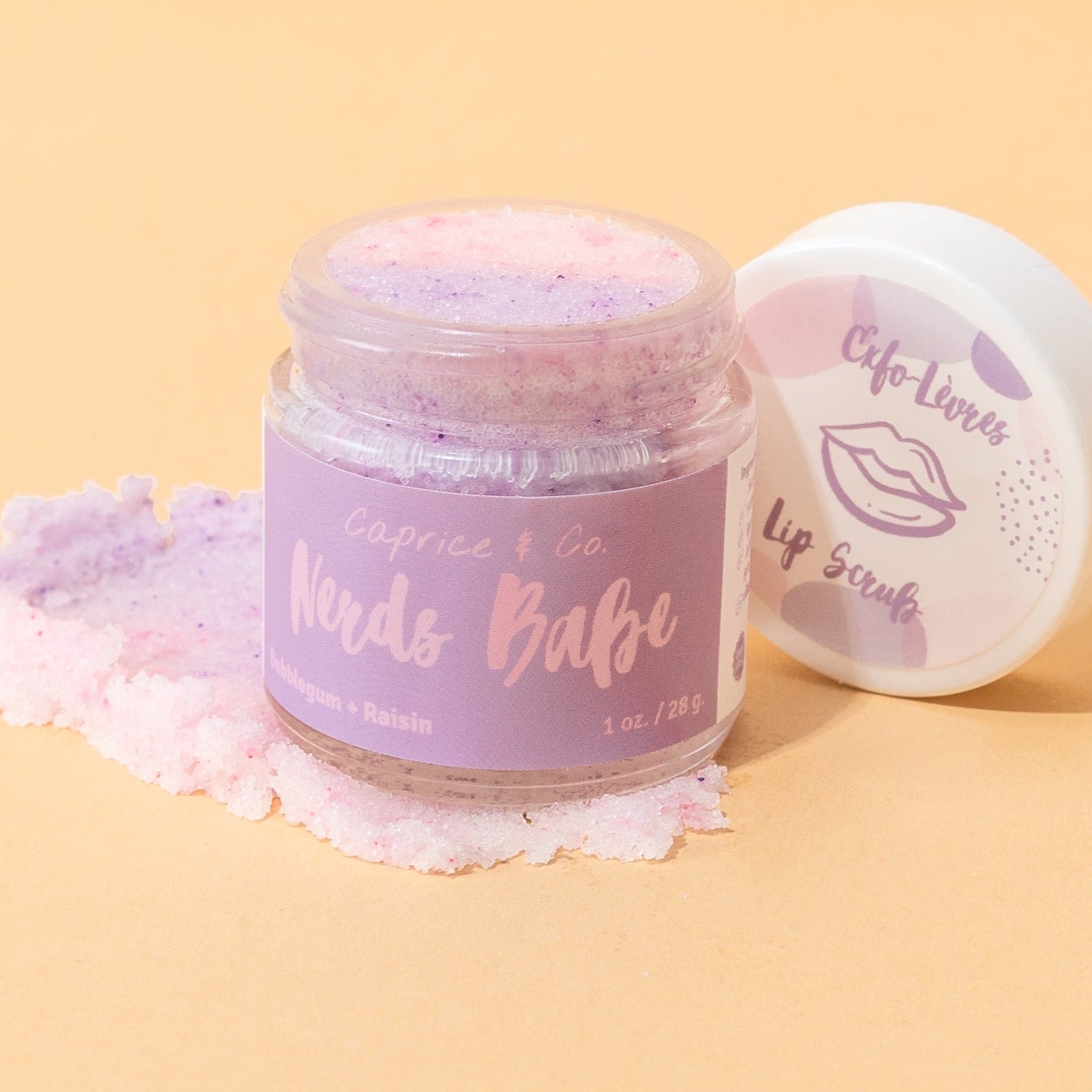 Nerds Babe Lip Scrub in a jar, featuring vibrant bubblegum and grape colors, with a spoon beside it for application.