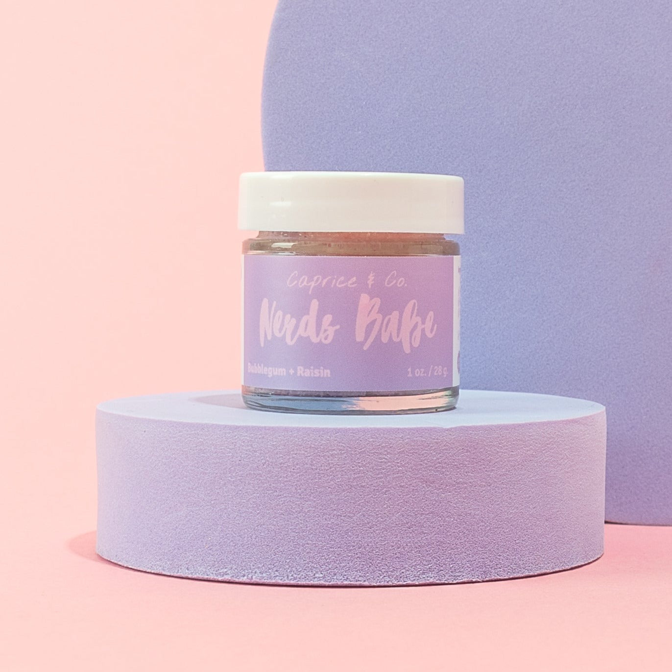 Nerds Babe Lip Scrub in a jar, featuring vibrant bubblegum and grape colors, with a spoon beside it for application.