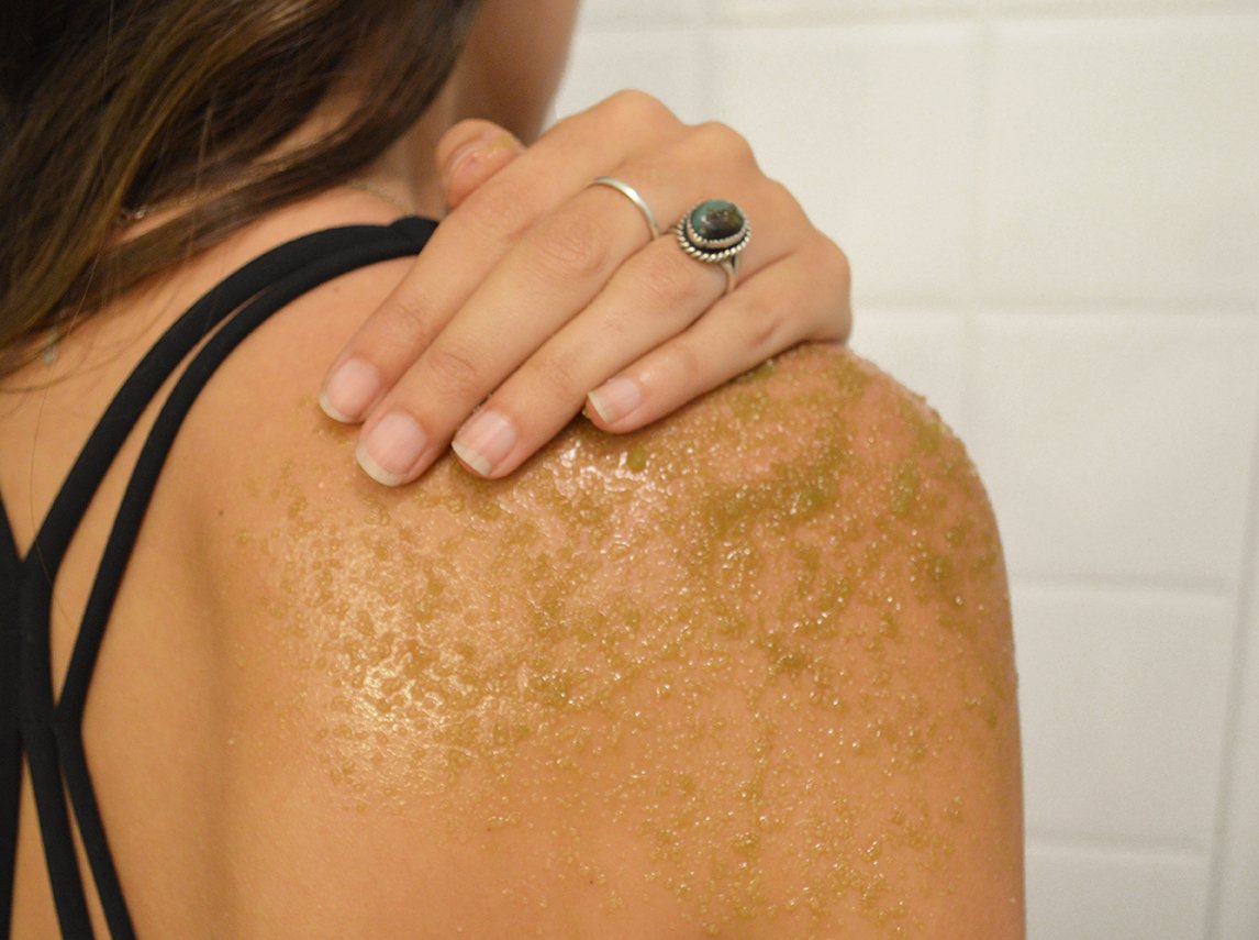 A jar of Matcha Sugar Scrub with a green scrub texture, surrounded by eucalyptus leaves and matcha powder.