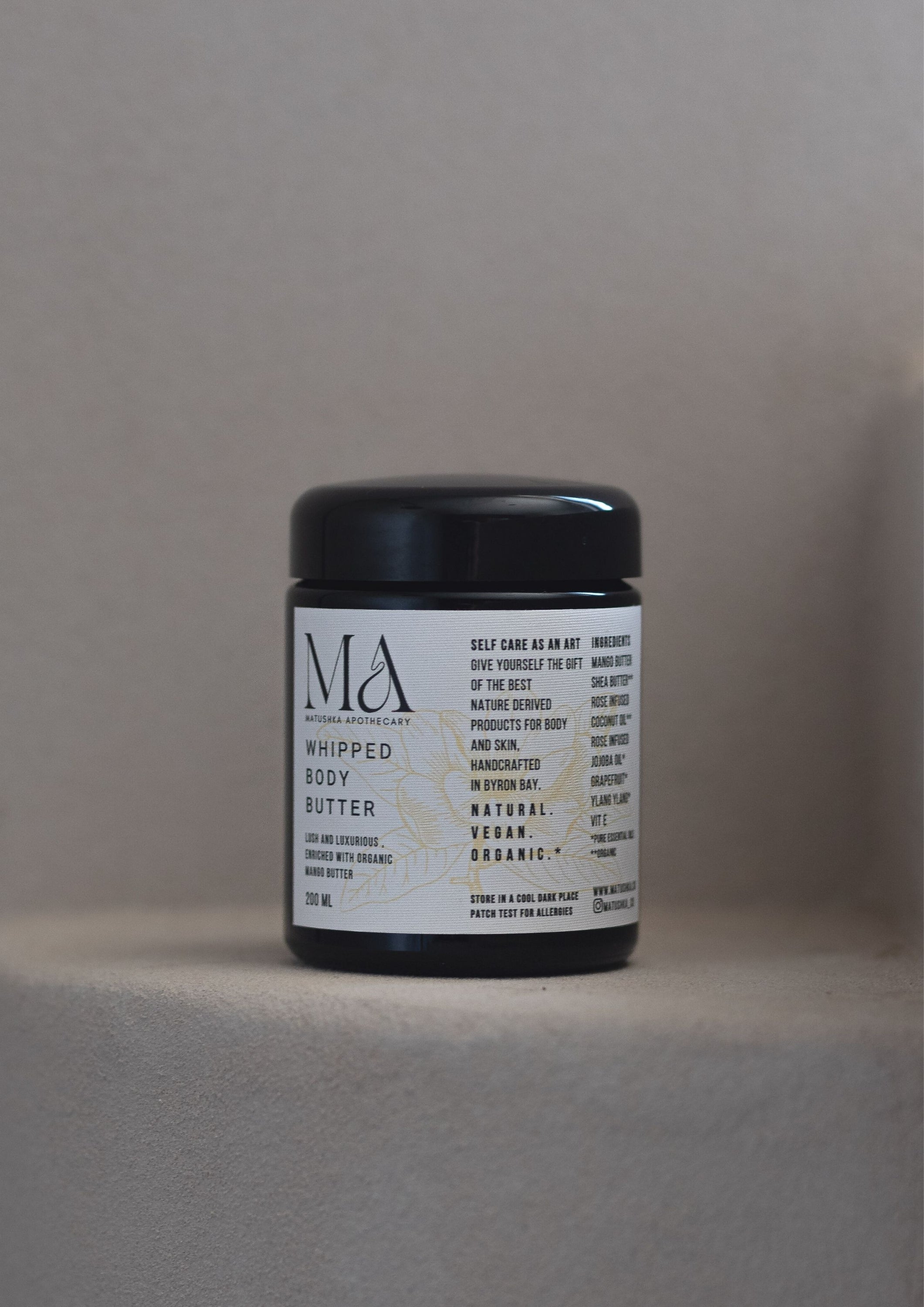 Matushka Organic Body Butter in a black miron glass jar, showcasing its creamy texture and rich ingredients like mango and shea butter.