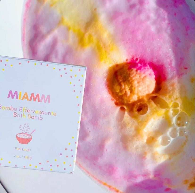 Miamm Bath Bomb in vibrant colors, shaped like a sphere, with a label indicating Fruit Loops scent, resting on a wooden surface.