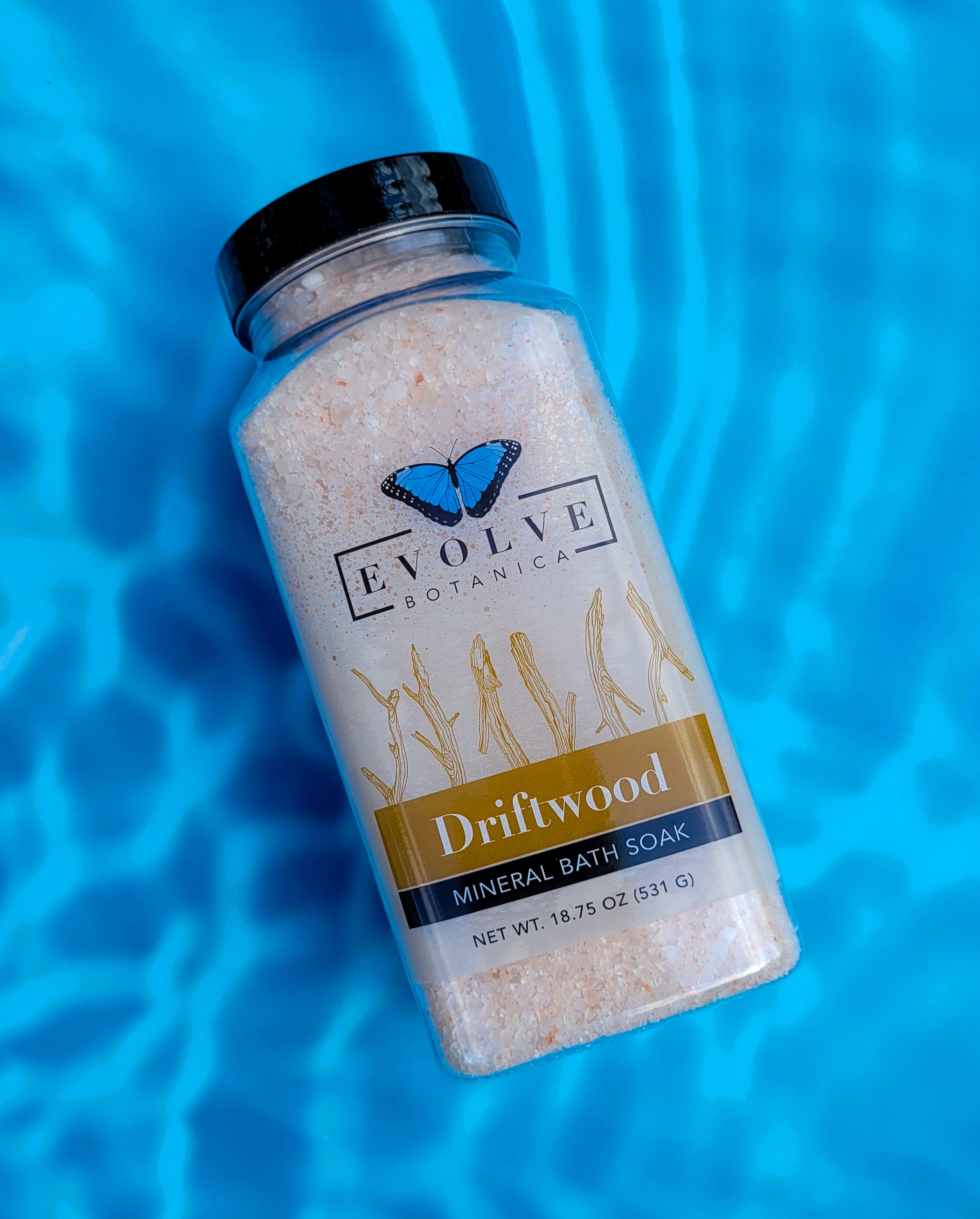 A jar of Mineral Soak - Driftwood bath salt, showcasing a blend of pink and white salts with a rustic wooden lid.