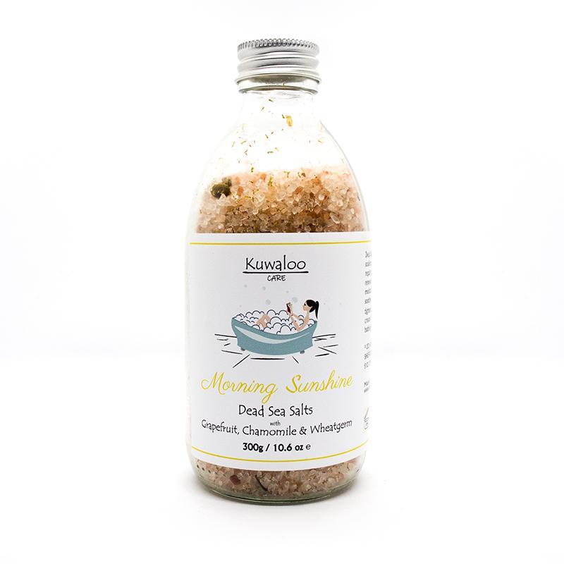 A jar of Morning Sunshine Bath Salts containing mineral-rich Dead Sea salts, surrounded by fresh grapefruit and wheatgerm oil ingredients.