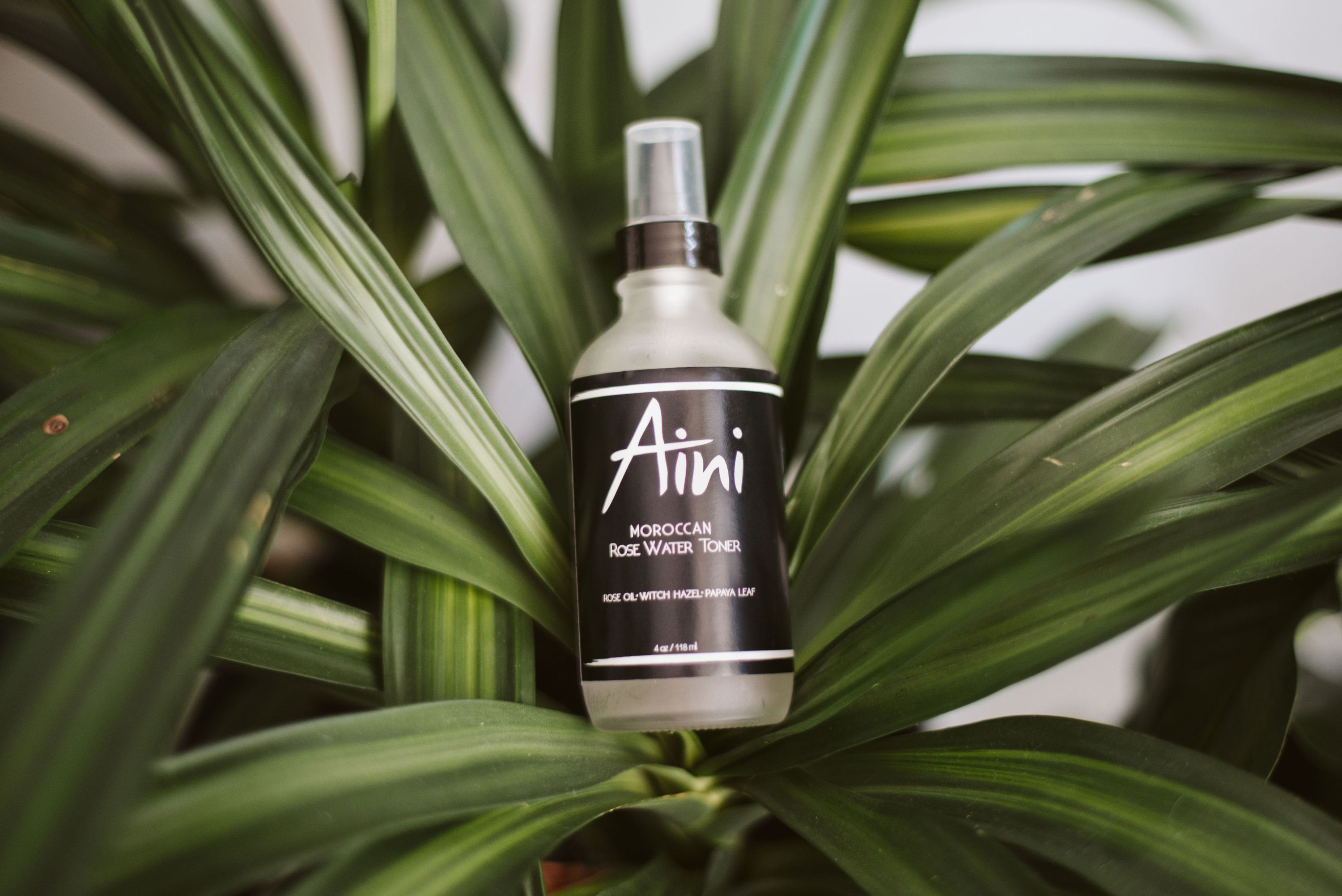 A bottle of Moroccan Rosewater Toner with a floral design, surrounded by fresh roses and papaya slices.