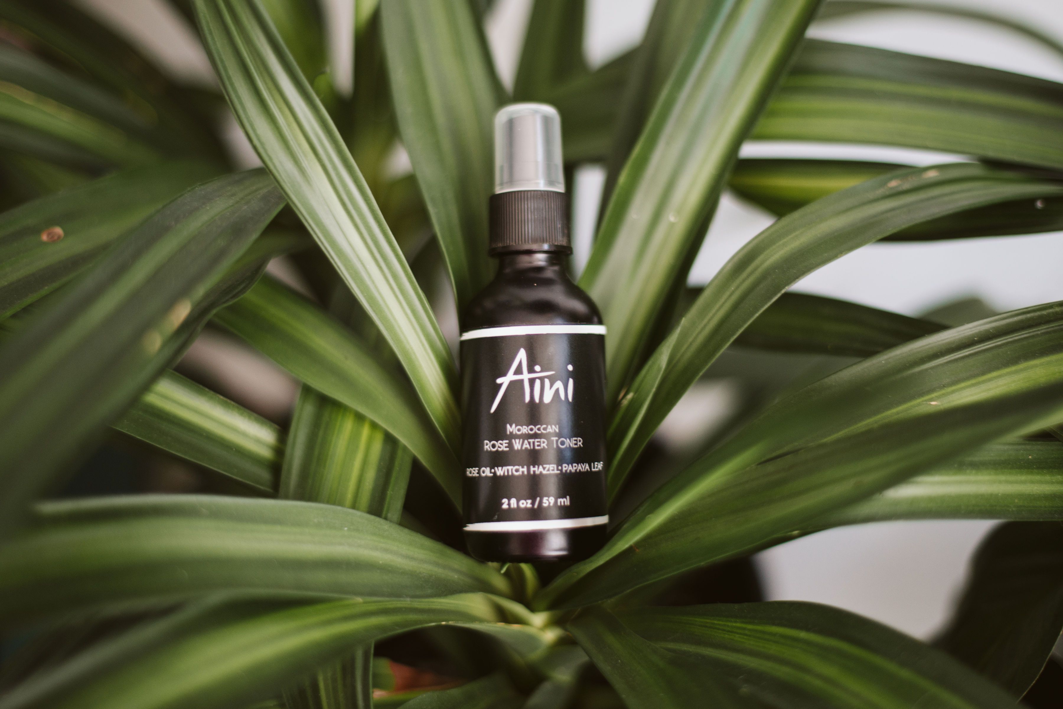 A bottle of Moroccan Rosewater Toner with a floral design, surrounded by fresh roses and papaya slices.