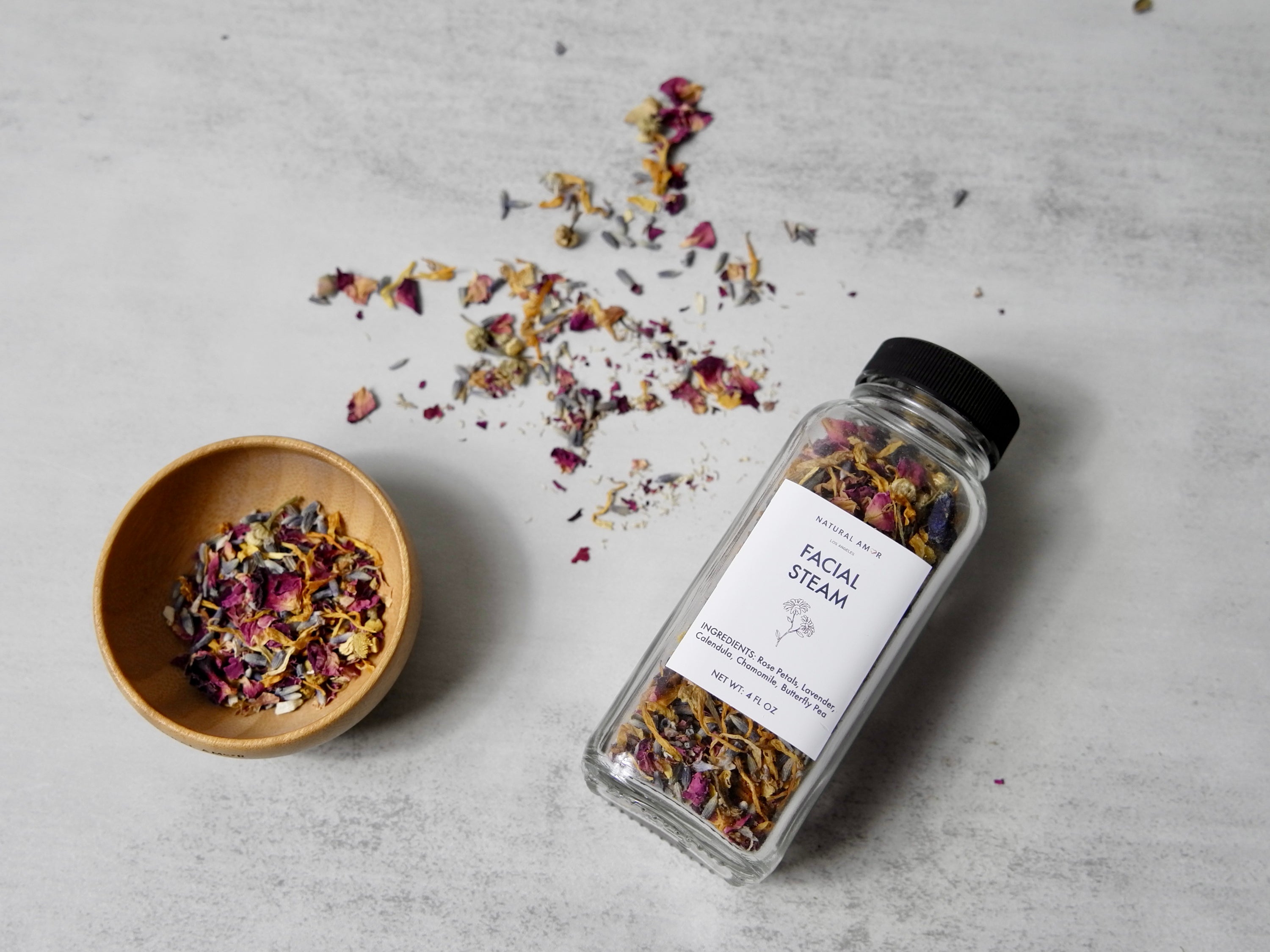 A 4oz glass jar filled with a colorful blend of organic herbs and botanicals for facial steaming, including rose petals and lavender.