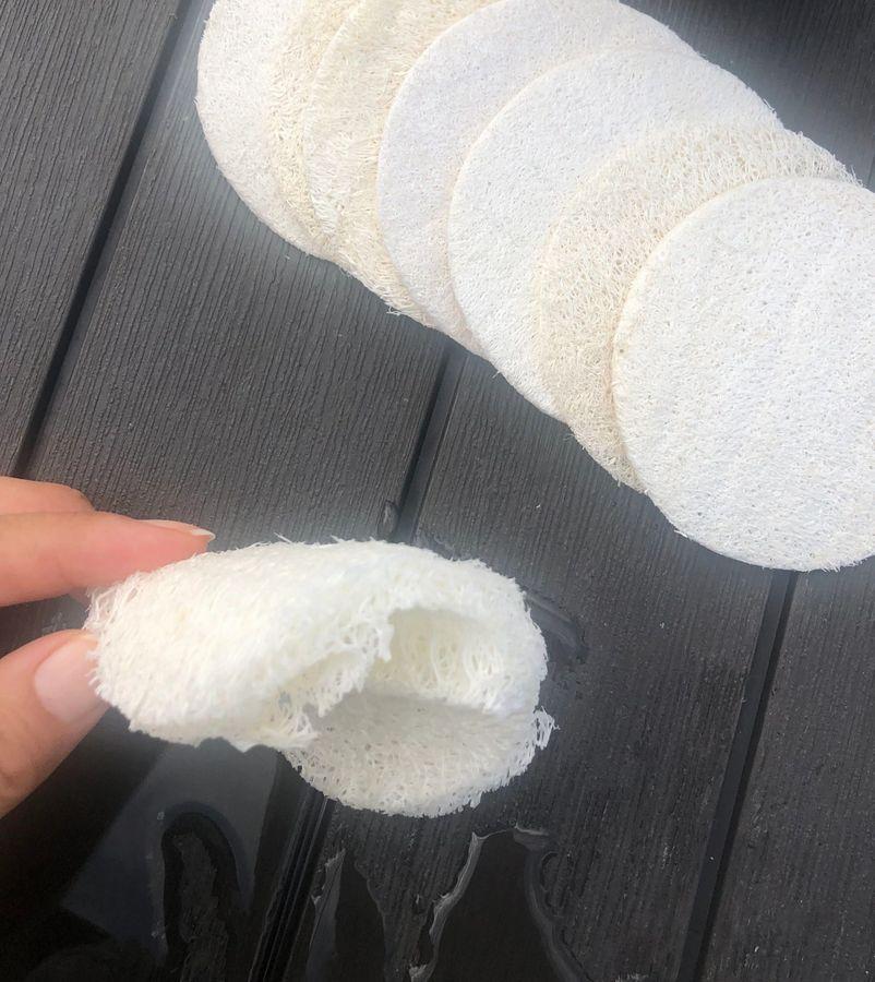 Five natural loofah pads in a pack, showcasing their off-white color and circular shape, ideal for exfoliating skin.