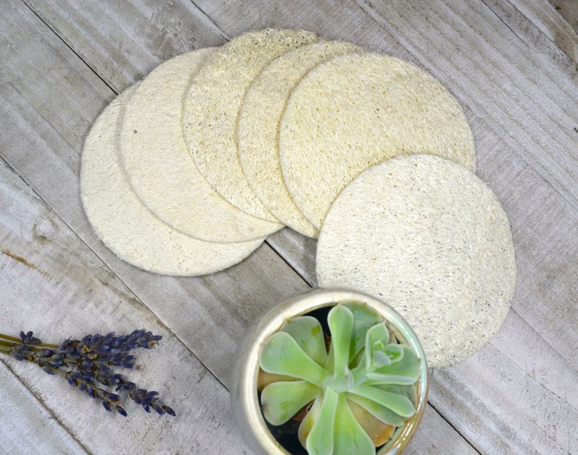 Five natural loofah pads in a pack, showcasing their off-white color and circular shape, ideal for exfoliating skin.