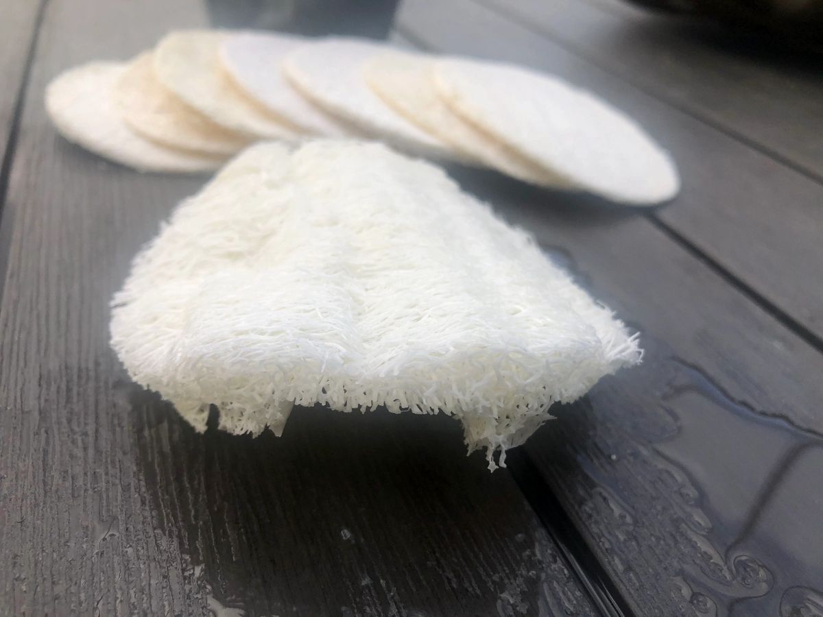 Five natural loofah pads in a pack, showcasing their off-white color and circular shape, ideal for exfoliating skin.