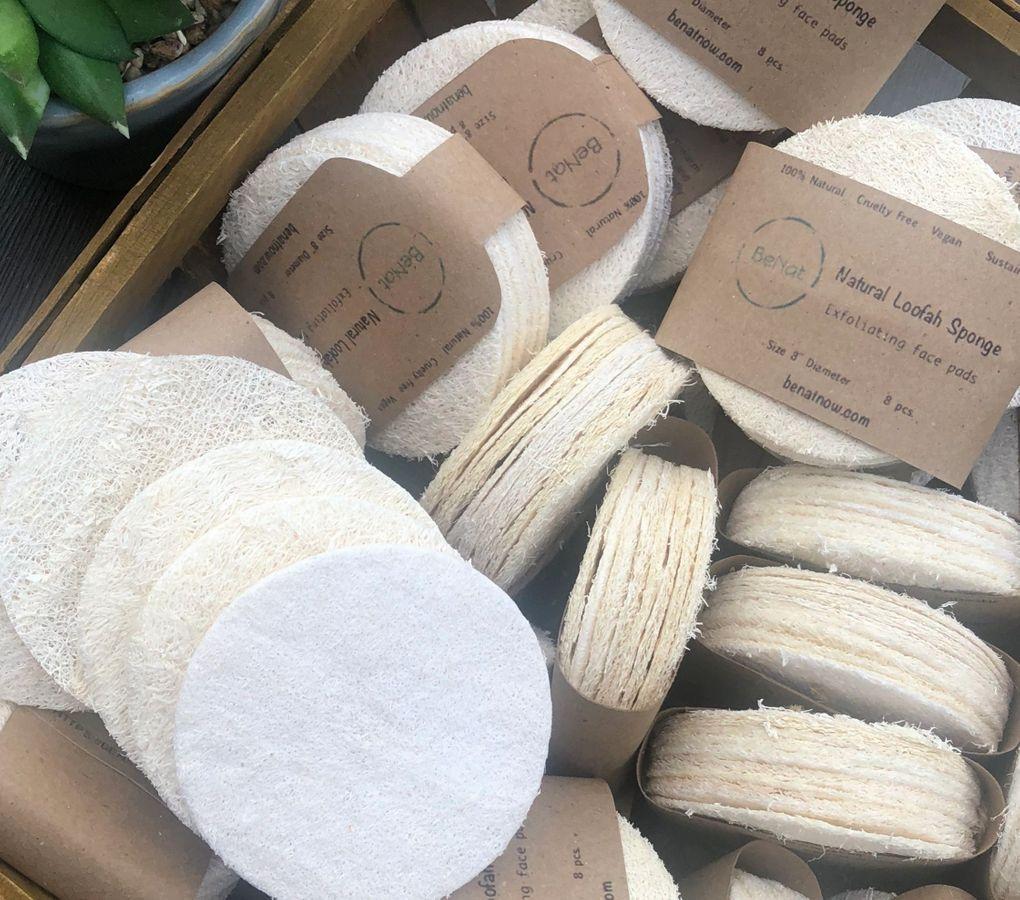 Five natural loofah pads in a pack, showcasing their off-white color and circular shape, ideal for exfoliating skin.