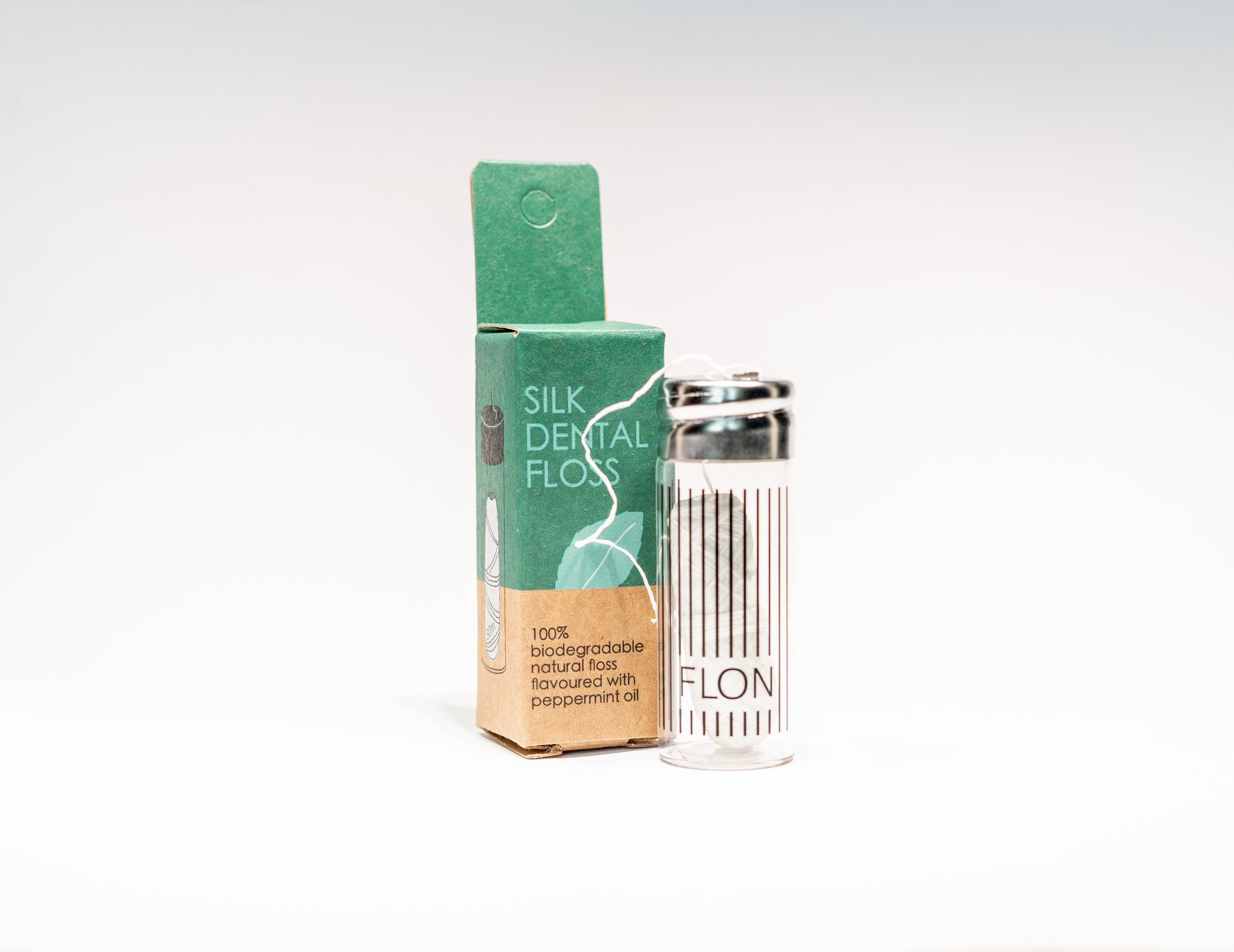 Natural Silk Dental Floss in a reusable glass dispenser with a metal cap, featuring a strong silk thread coated in Candelilla wax and peppermint flavor.